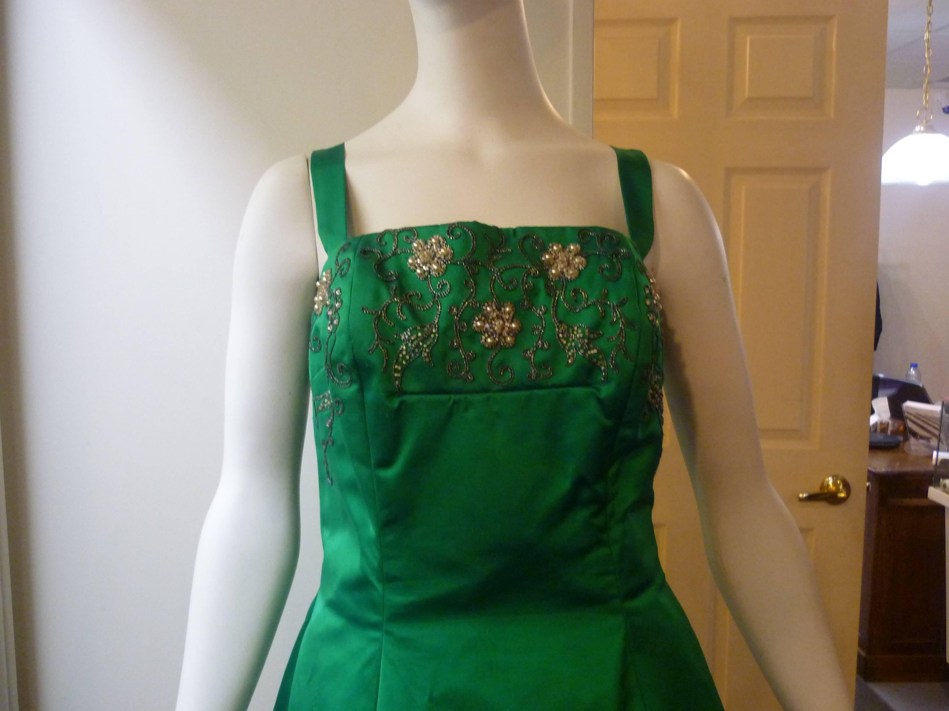 As seen in Vogue (England) in 1963, this is a beautiful emerald green satin gown adorned with metal thread work, as well as beadwork (bugle beads, pearls and sparkling crystals). These are all embroidered directly to the gown by hand.

The tailor