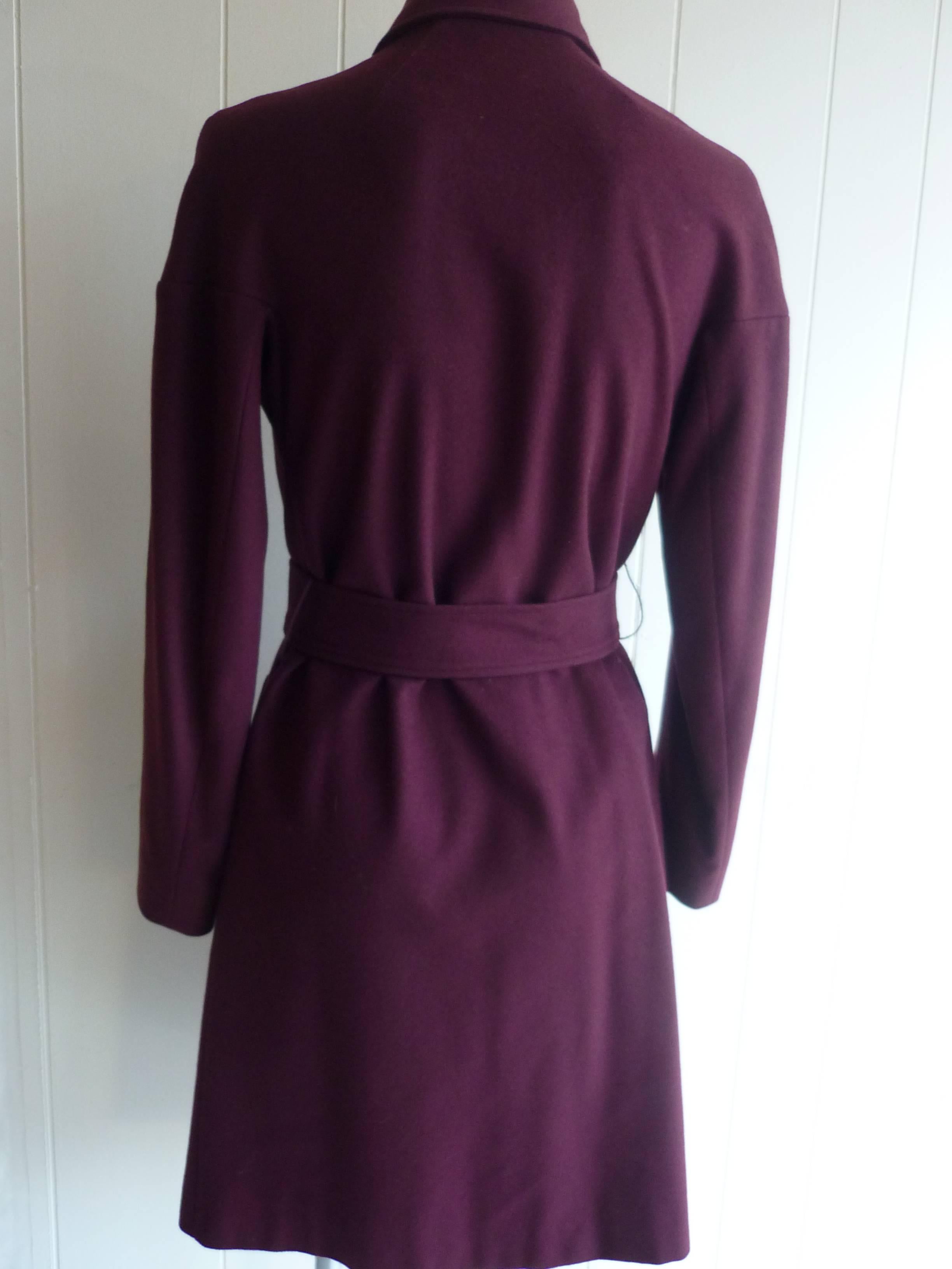 Lovely burgundy colored wool belted wool coat, features notched lapels, magnetic closure at front, as well as eye and hook closure and magnetic button at neck if you want complete coverage. There are also two slit side pocktets. Made in France.
