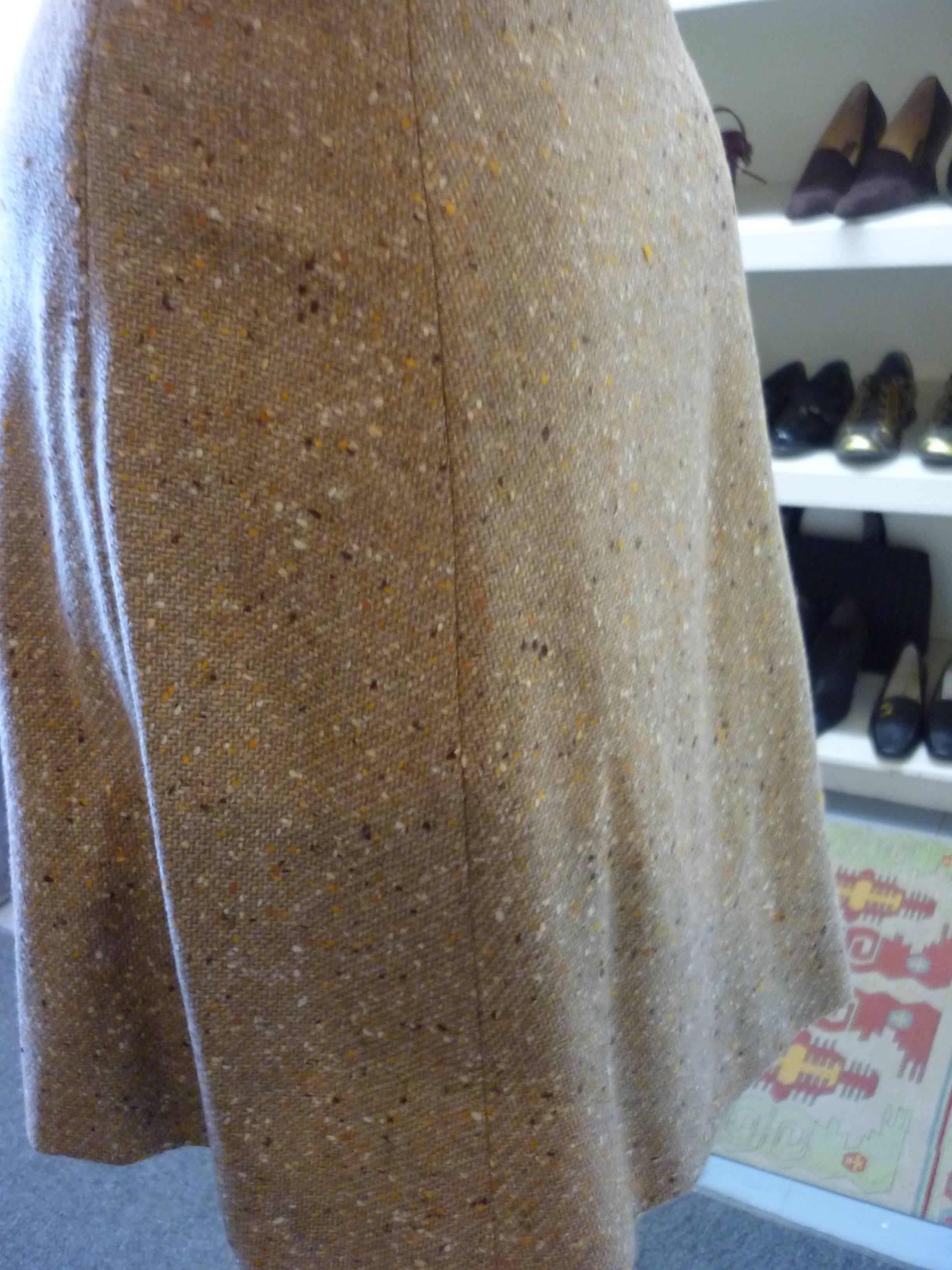 Very nice a-line wool tweed skirt in tones of beige with a hint of orance. Thre is a pleat on the fron which give the impression of a wrap skirt; a big button with a quarter belt; zip closure on the side, and the hem is hand finished.