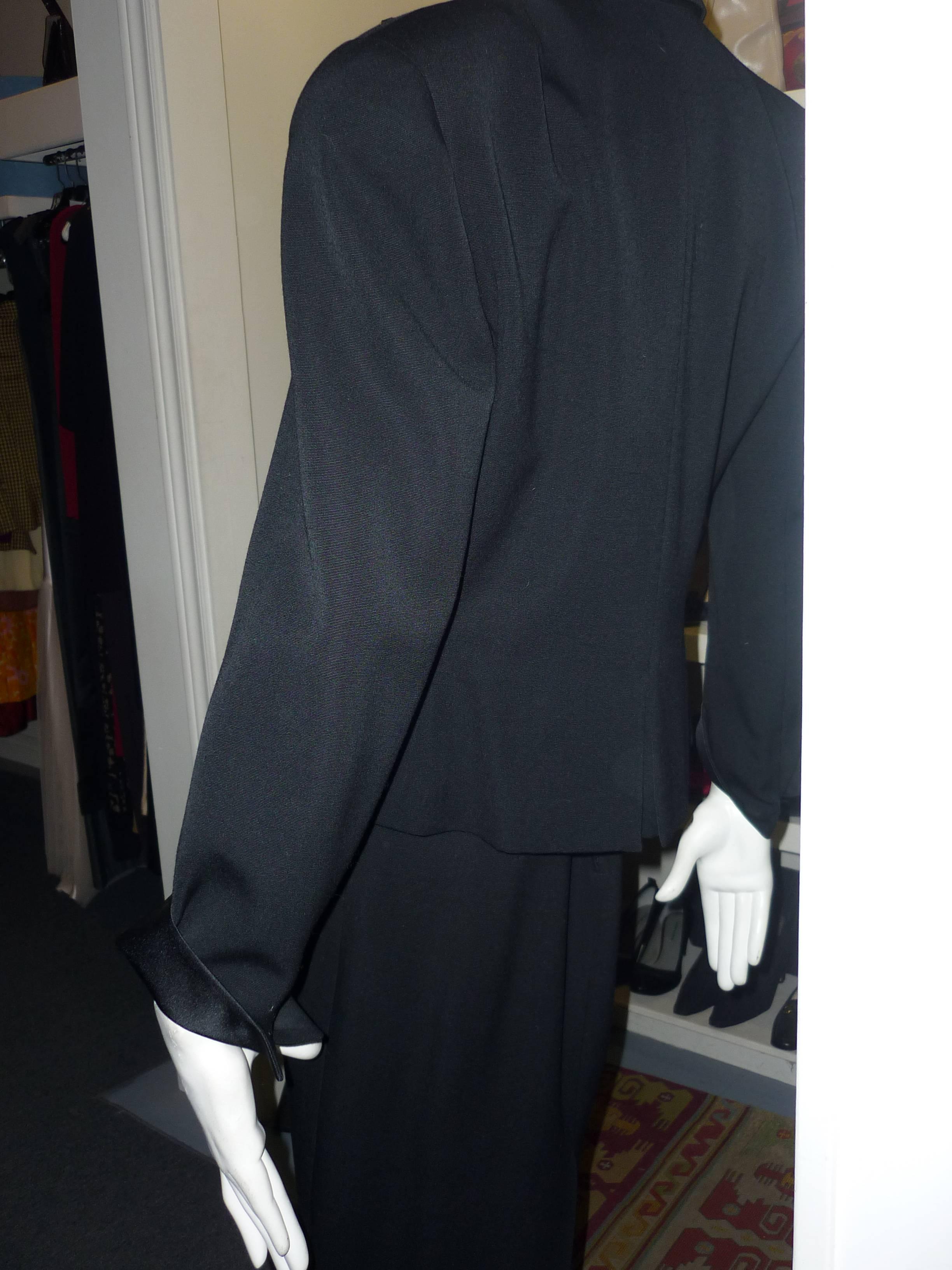 This lovely suit comprises of a tuxedo jacket with a peplum look and a fake back slit; satin lapels/cuffs and cufflink closure, a satin vest with six gold and black buttons, and a pencil skirt with slit side pockets. 

This is Christian Dior 