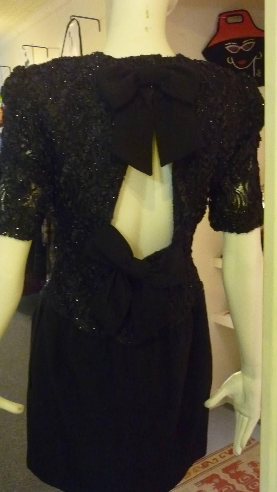 This dress has a dropped waist wool skirt with side slit pockets, and a combination ribbon, net and metallic top. The back is a surprises in that it has a keyhole opening and two beg bows. 

As it is a 1980s it has shoulder pads