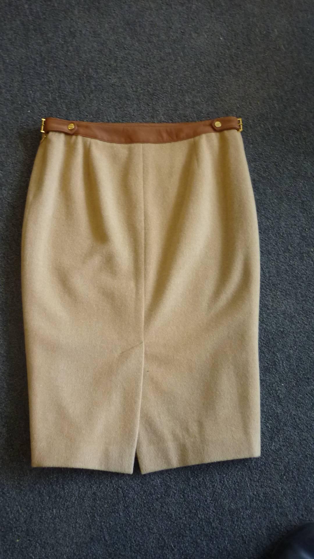 Beautiful pencil skirt with a leather waist band and gold buckle detail on the sides. The skirt is camel colored with a contrasting tan leather waist band. There is a small centre back slit and a side zip.