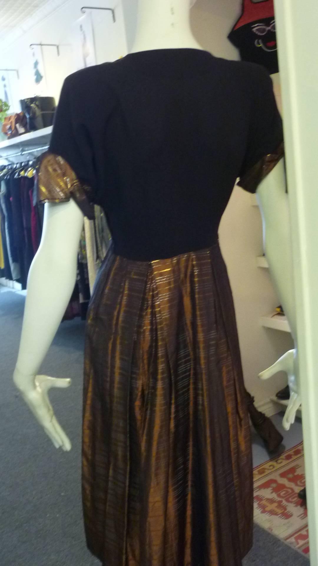 Black crepe top and bronze and gold metallic rayon or acetate make up this lovely dress. The metallic pattern is also replicated on the short sleeve cuffs with bows and the two button closure at the neck. There is soft shoulder
