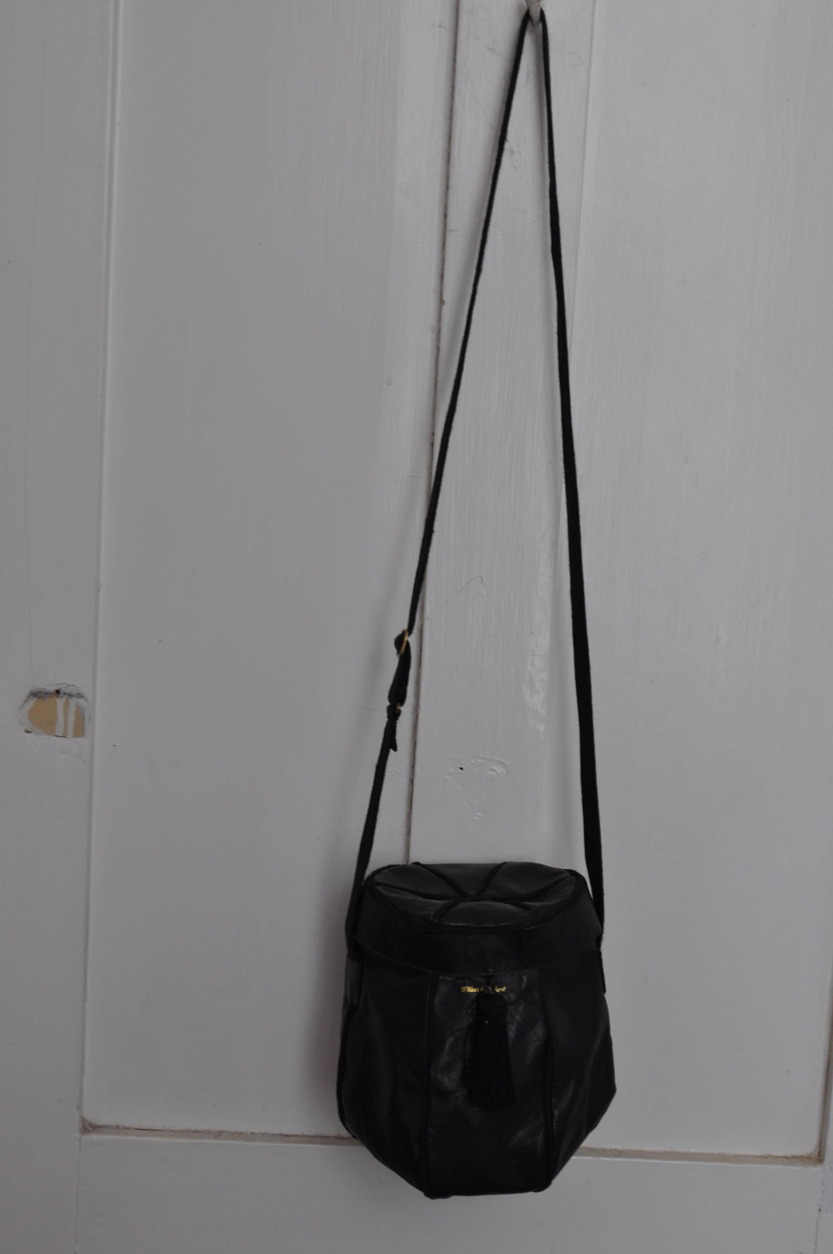 This may be a one of a kind purse ordered by the Wilkes Bashford store. It is black; made of a coated material which resembles the texture of lizard;  grosgrain borders; a clasp closure with a tassel, and a ribbed material adjustable crossbody