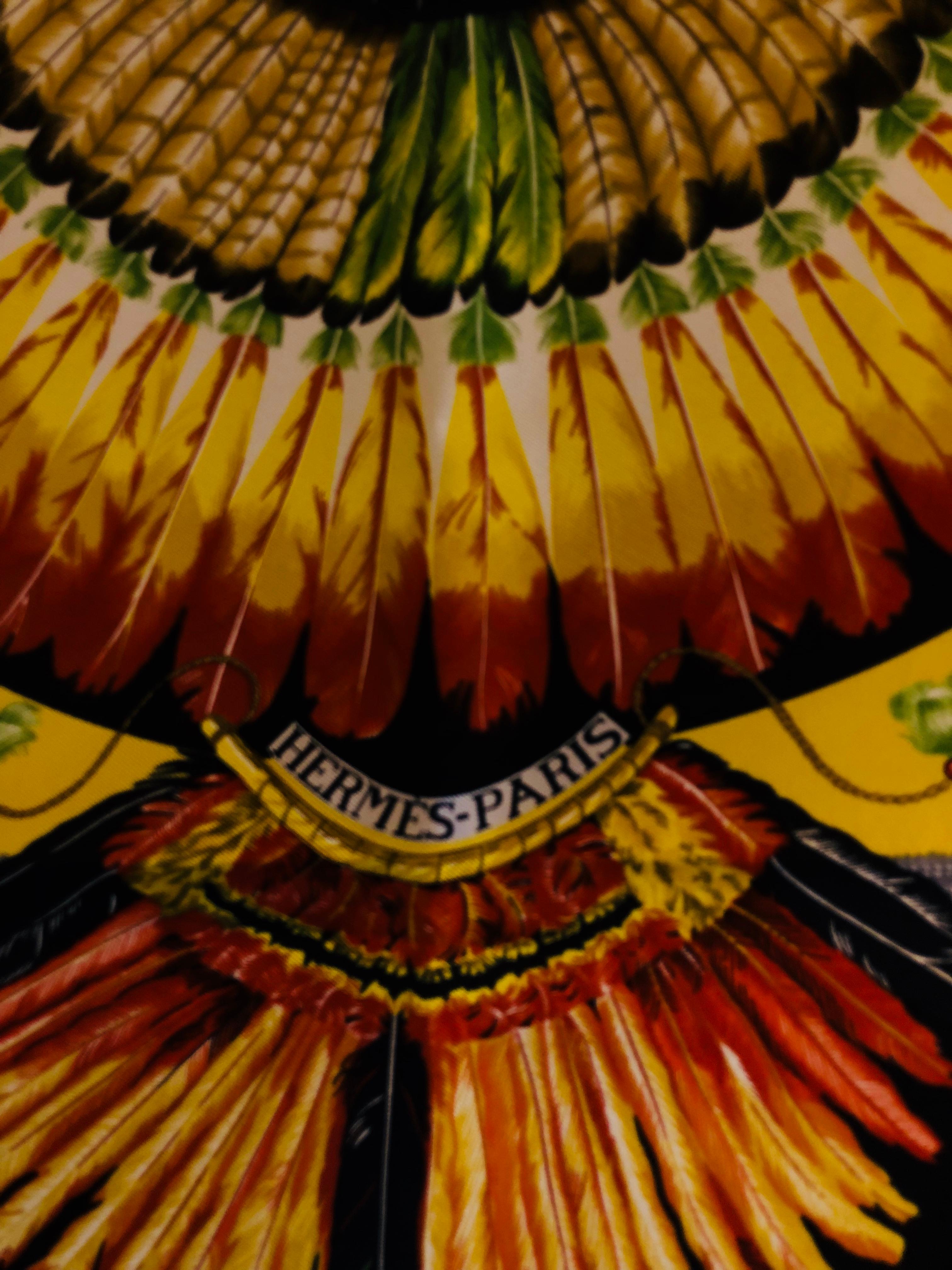 Designed by Laurence Bourthoumieux, this 1988 silk twill scarf features graphics indigenous to Brazil such as feathers, beads, head pieces and wood.

The colors are brilliant, with a yellow background and oranges, greens, grey, white and black. The