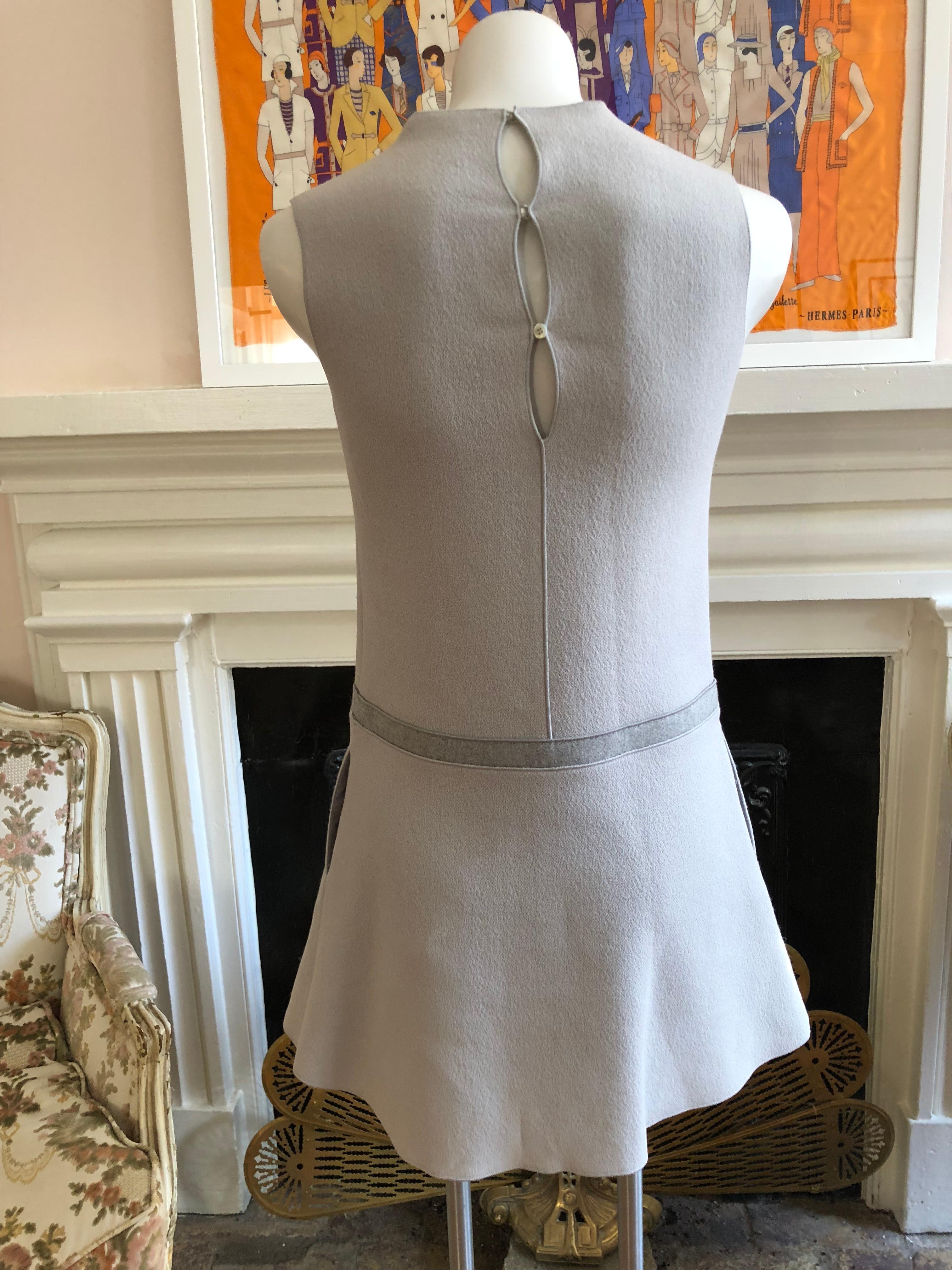 Stunning tailoring! This light grey fleece wool and silk a-line dress has a very nice architectural collar; front pleat; felt band around the hip and two slit pockets. Back closure is by way of three buttons.

This dress will take you from work to