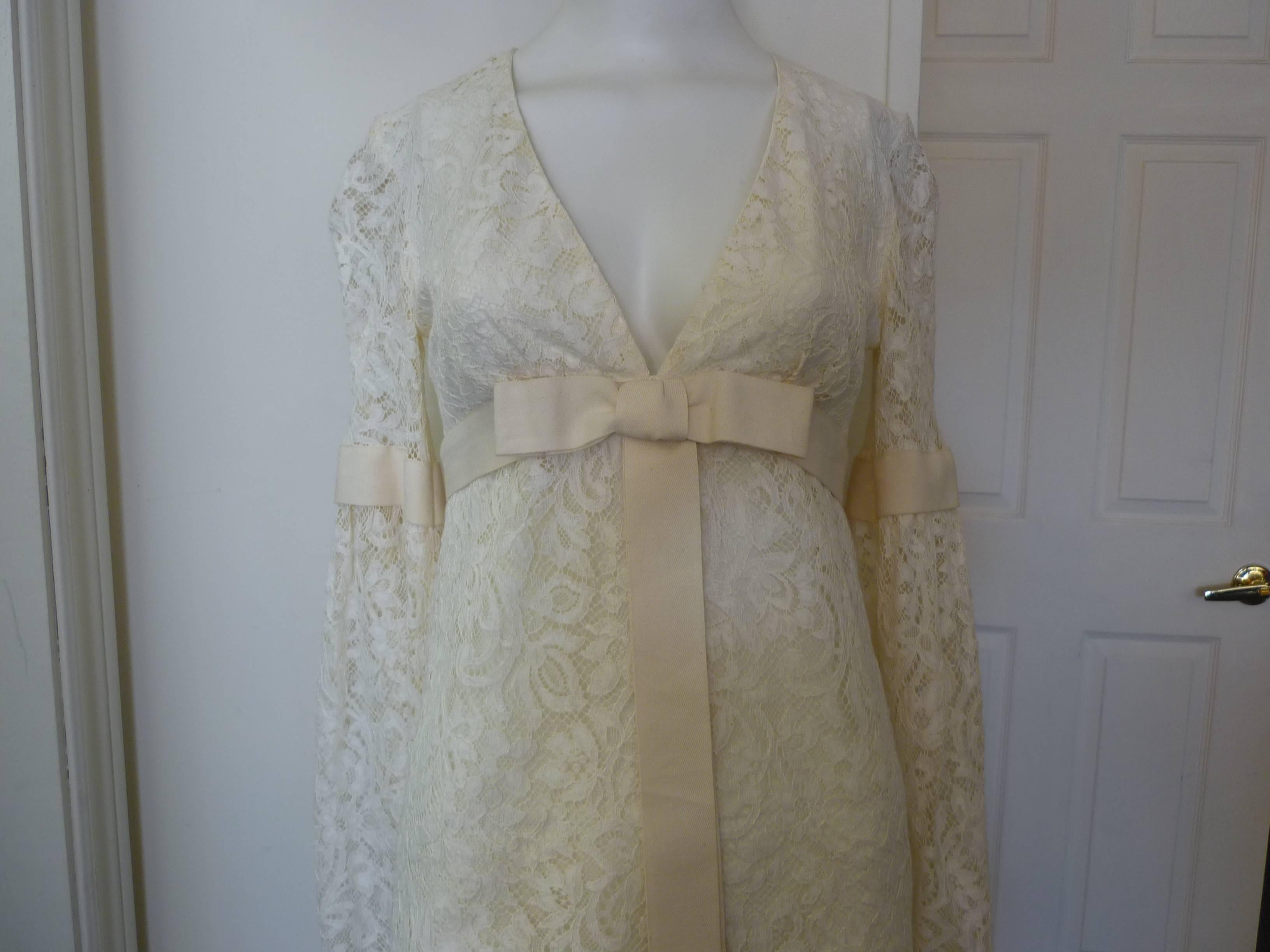 Lovely Ivory v-neck lace mini dress, with an empire waist and a grosgrain tonal trim and bow under the bust.

The dress has bell sleeves with the same tonal trim, and the hem is scalloped.