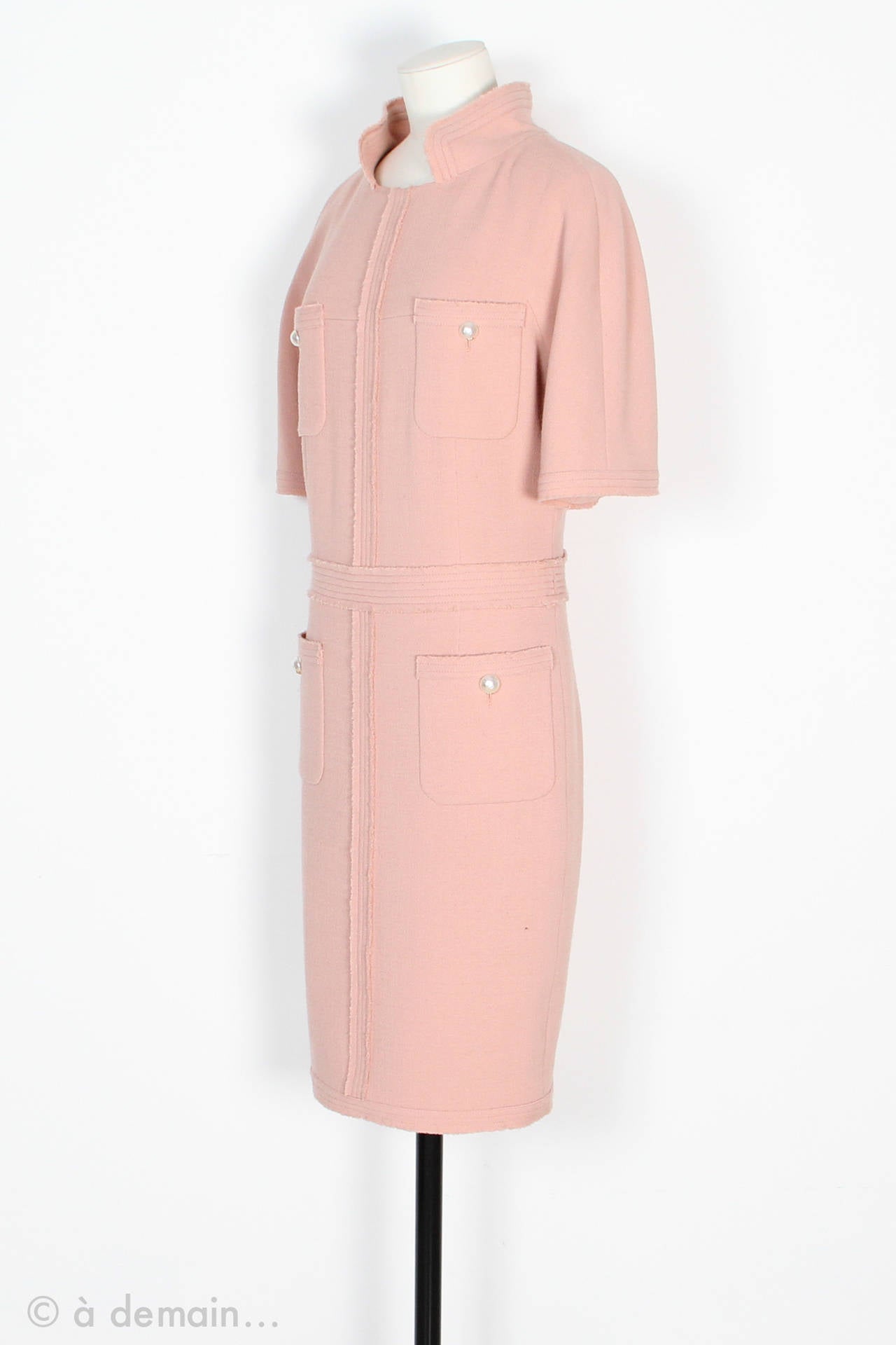 Chanel Dress made in France in pink wool and lined with pink silk. Short sleeves. 4 pockets closed by a large pearly button with the famous X on it. Matching waistband sewn on the dress. Zip on the bottom of the skirt to hide or show the legs. Zip