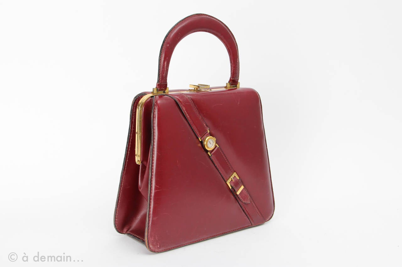 Rare 1960s Fernande Desgranges Handbag with a watch on the front and one top handle. Burgundy color. Gold metal garniture. Made in France. Signed on the inside with 3 pockets (one zipped).
General good condition.
Some scratches and lacks on the