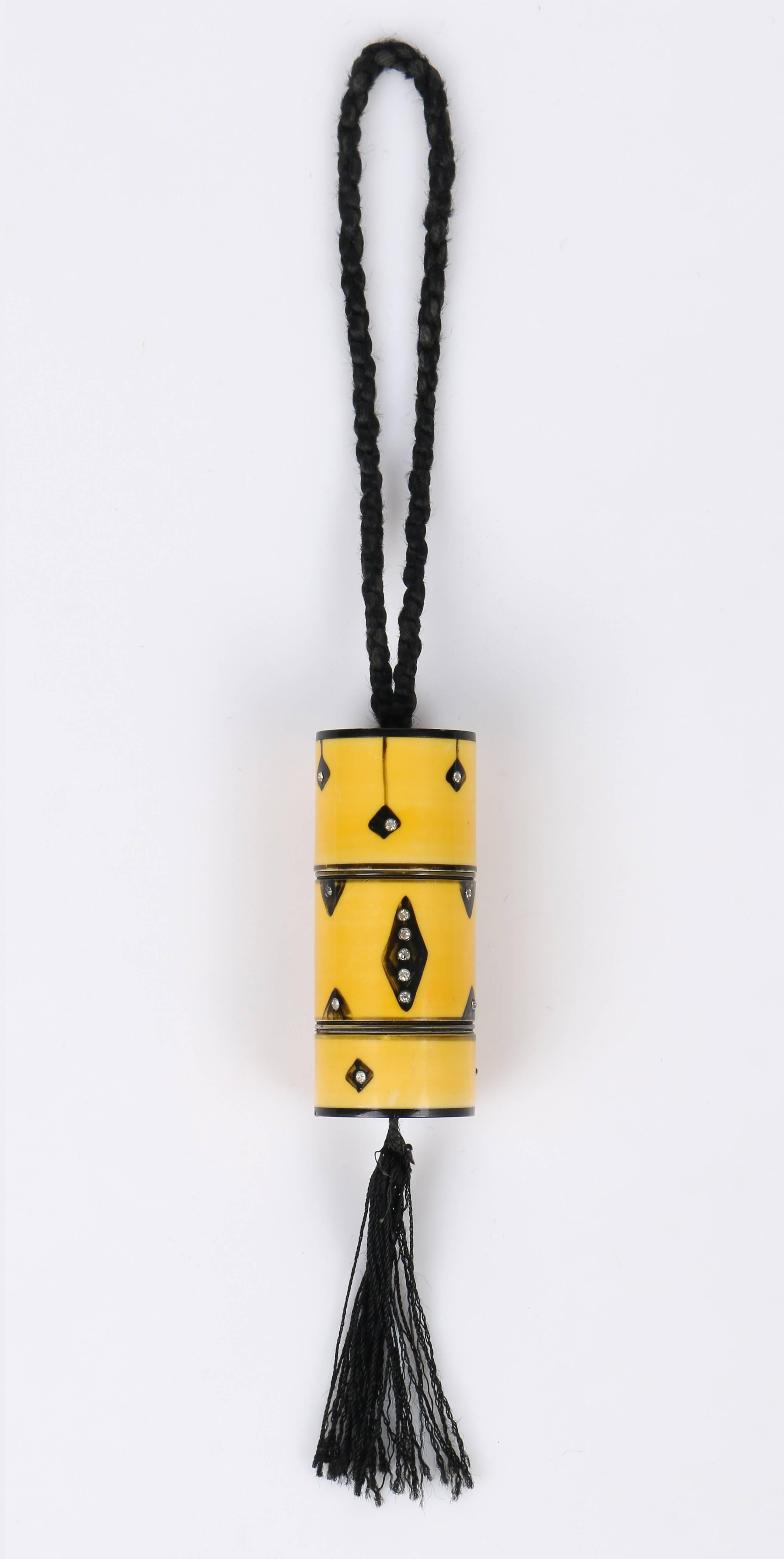 MUSEUM QUALITY: Arts & Crafts Era 1920's celluloid dance purse. Hand painted golden yellow with black geometric detail; silver rhinestone embellishment. Cylindrical shape. Black braided cord hand strap. Tassel detail at bottom. Bag unscrews into