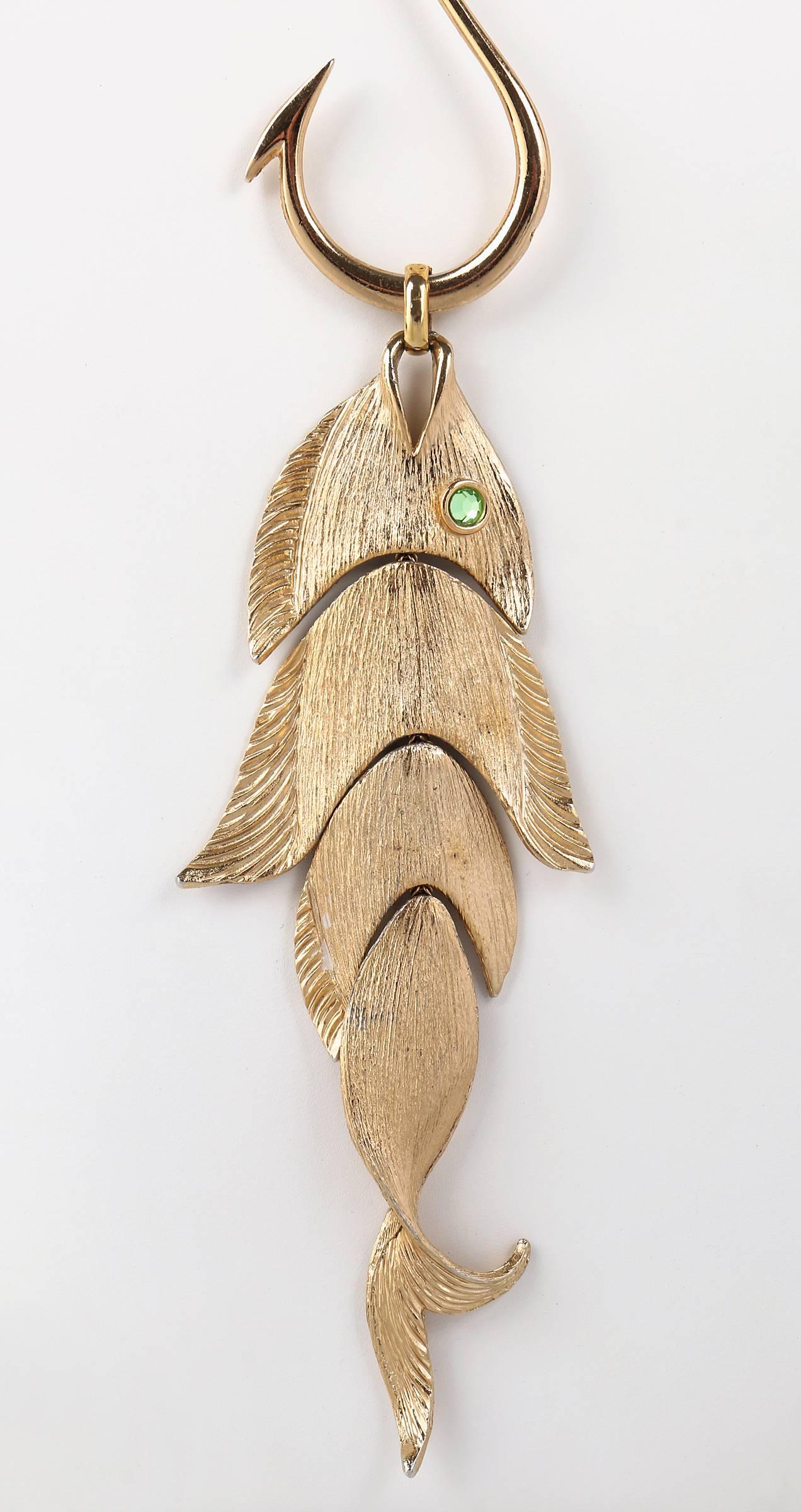 Vintage 1970's Napier statement gold tone fish on hook pendant on chunky gold tone chain.  Fish pendant is segmented into 4 pieces.  Matte gold tone is brushed and has carved detail.  Fish's eye is a faceted Peridot colored rhinestone.  Pendant