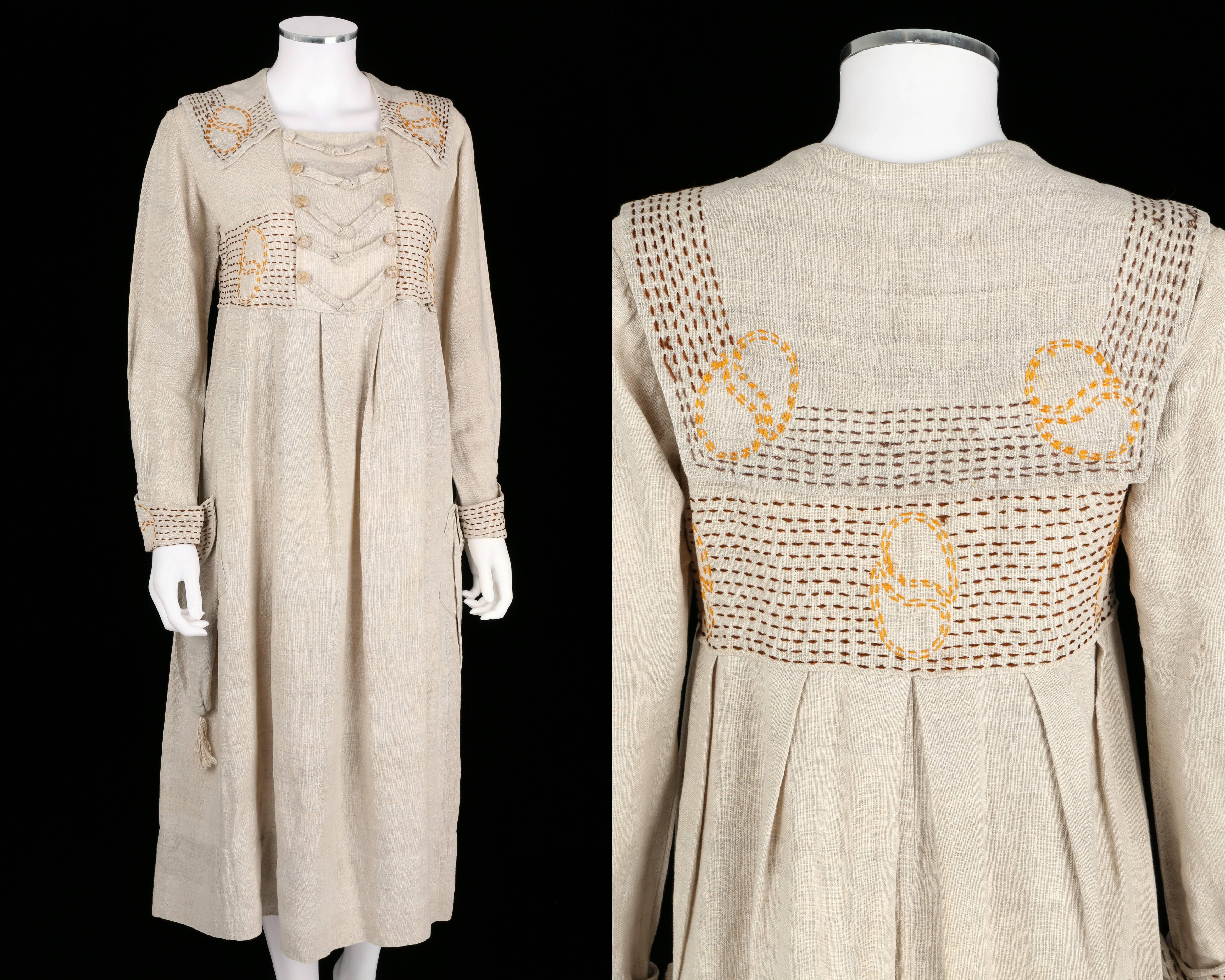 Vintage couture c.1910's natural linen rural smock frock dress. Brown and golden-orange hand embroidery on collar, waist, and cuffs. Two pockets with tassel trim. Front of dress closes with hooks and eyes at bust. Large embroidered sailor collar.