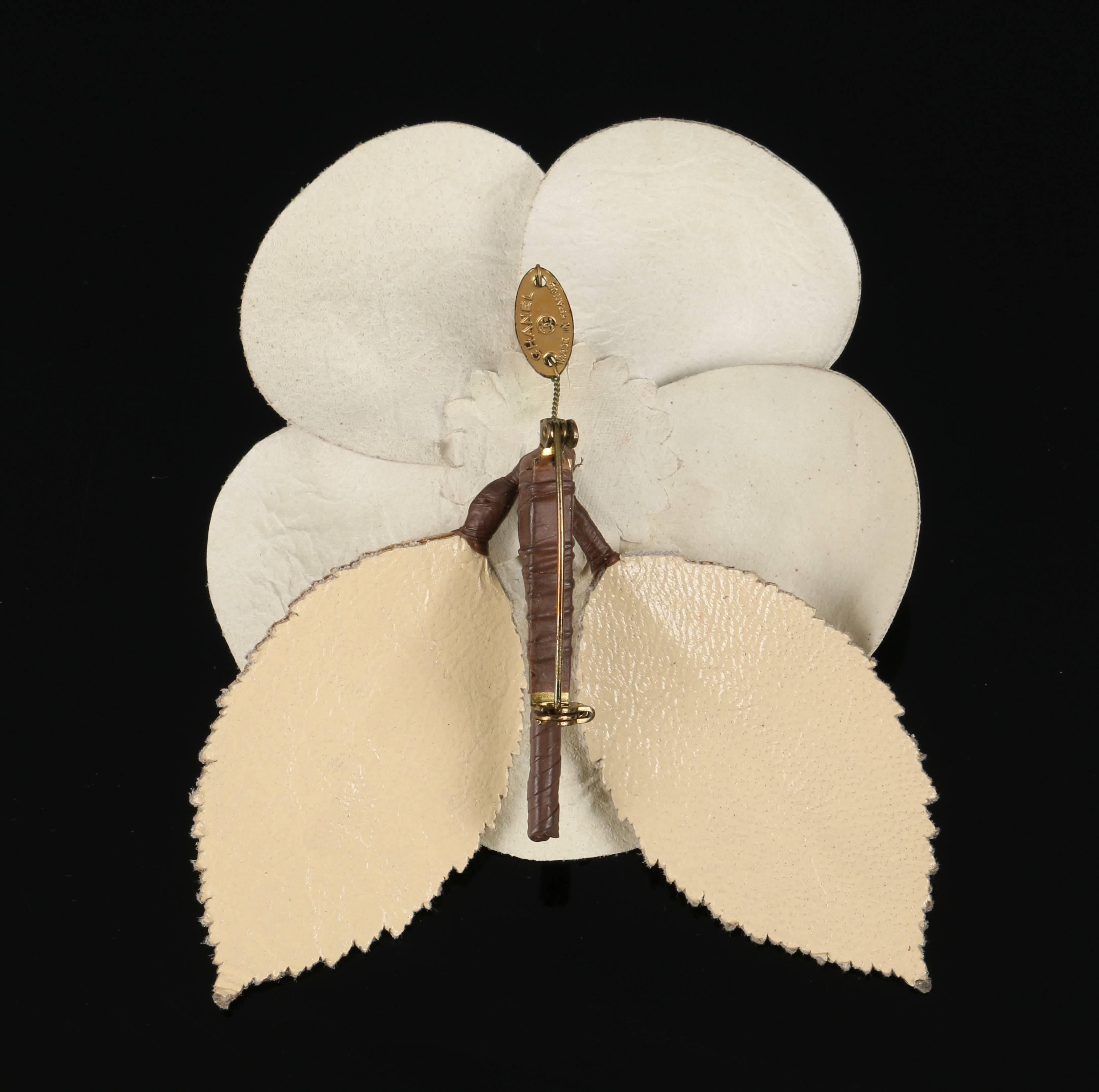 Chanel white leather camellia flower brooch. Gold (beige) leaves with cut leather leaf teeth detailing. Brown stem with needle clasp closure. Gold tag stamped with 