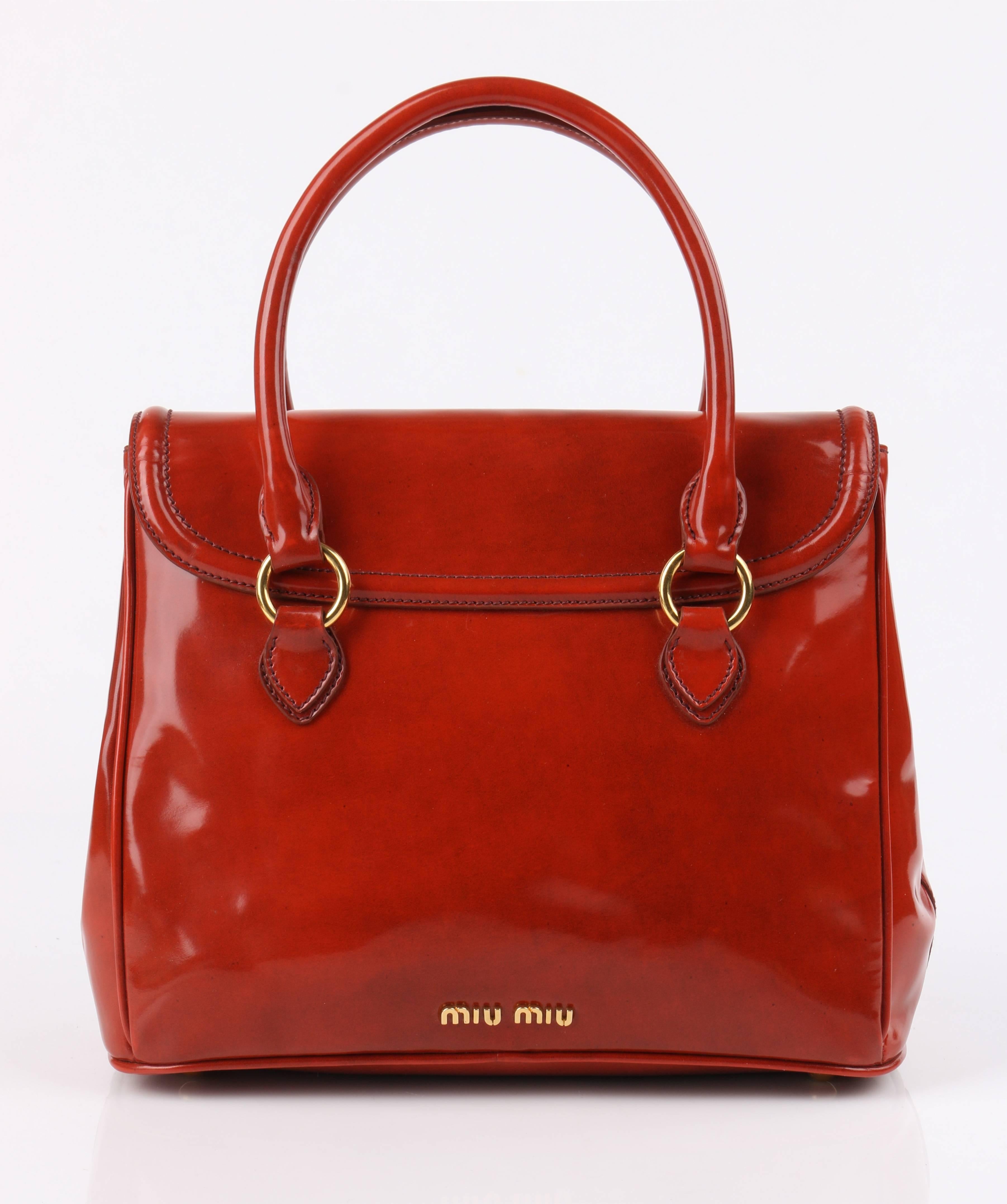 Miu Miu Prada Autumn / Winter 2012 burnt orange spazzolato (polished/patent) leather purse. Designed by Miuccia Prada. Burnt orange spazzolato exterior with piping detail. Flap top with gold-toned metal slide lock closure. Two single rolled handles