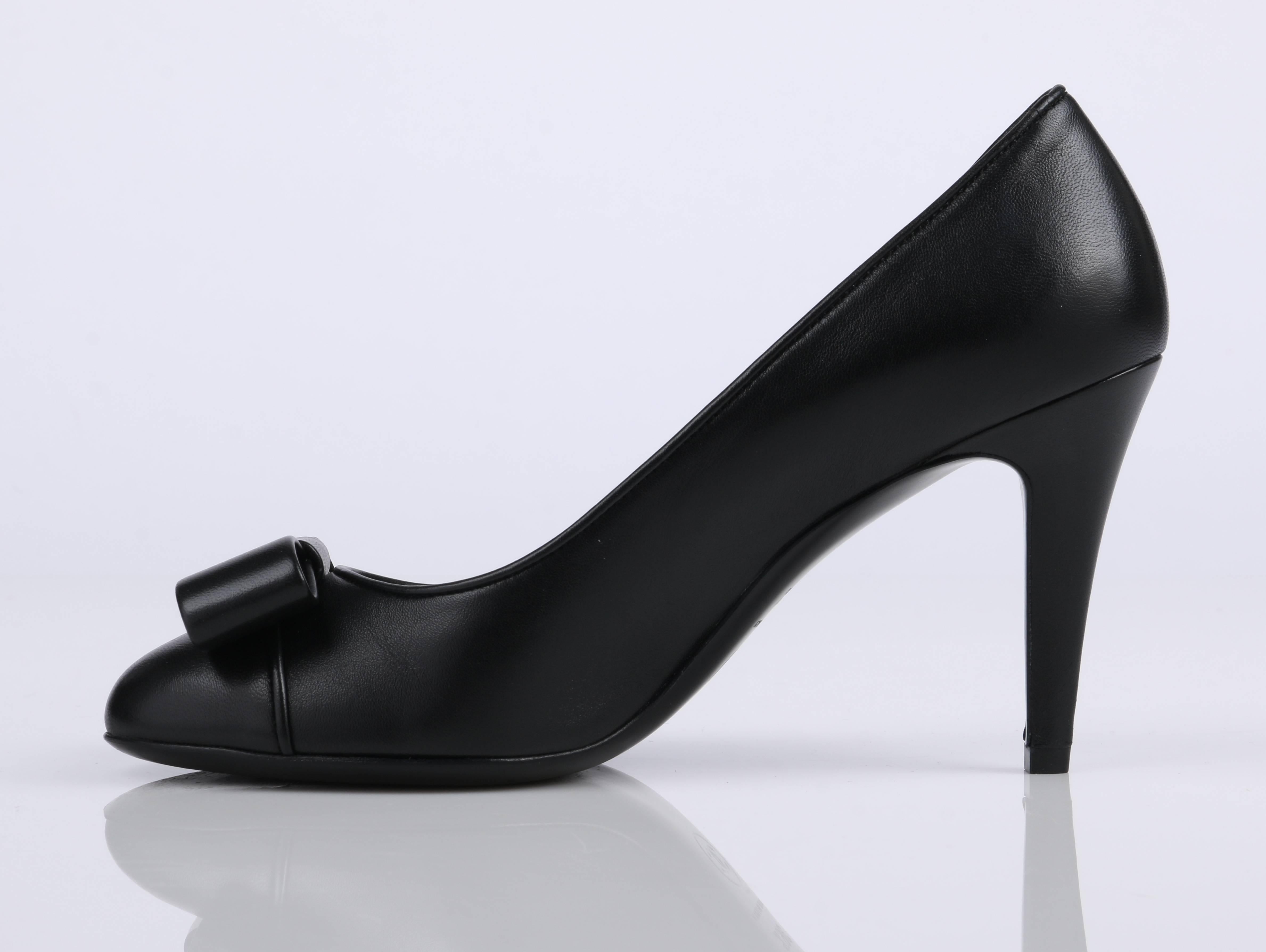 Chanel S/S 2015 classic black leather heels. Smooth black leather with black leather cap toe. Rounded toe detailed with contemporary flat black leather bow. Outside heel detailed with small silver tone 