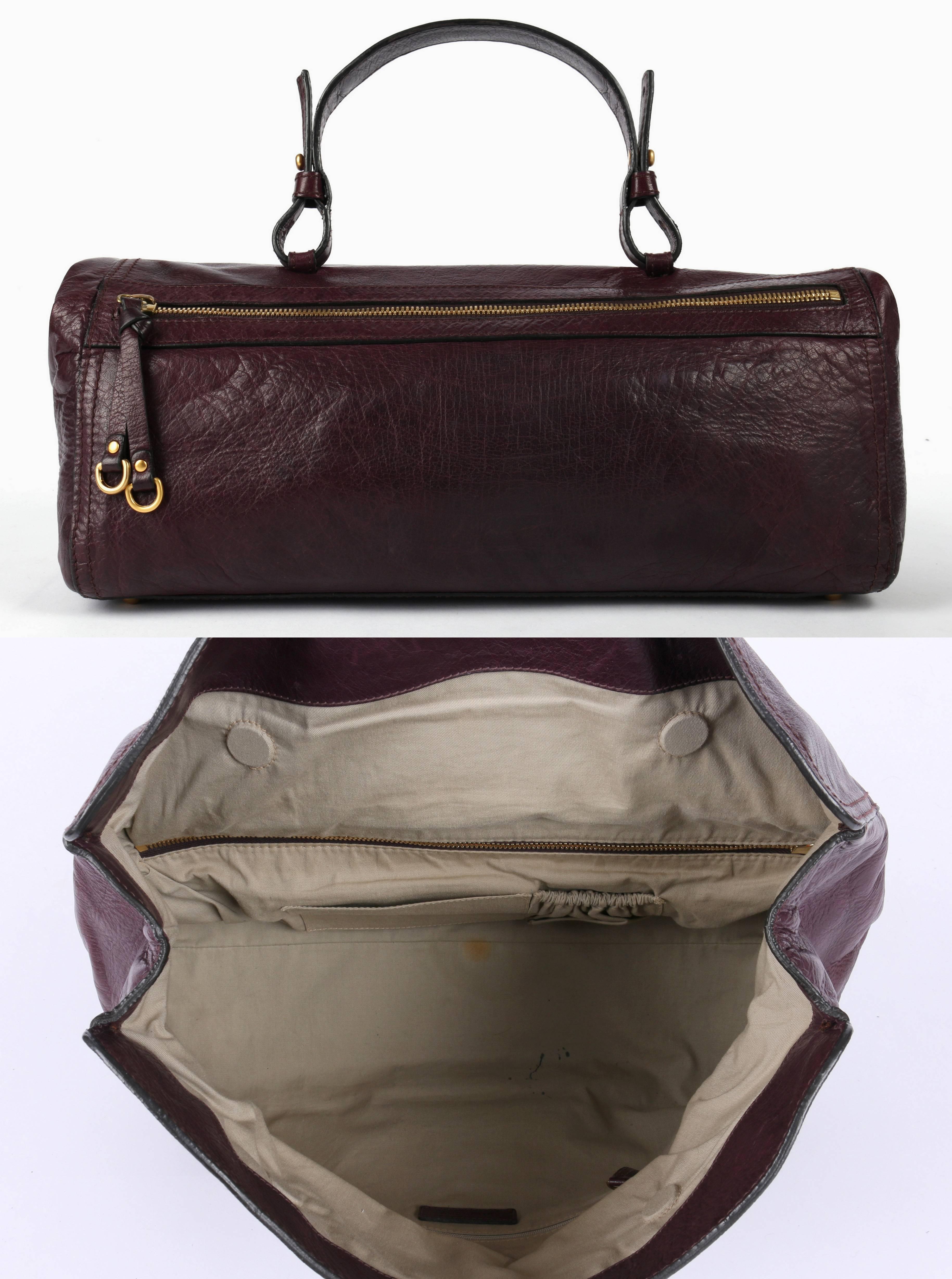 Givenchy c.2007 plum purple genuine leather east-west buckle bag. Adjustable flat leather top handle. Fold-over design with central gold-tone buckle closure. Dual hidden interior magnetic closures. Exterior back zip pocket. Protective gold-tone base