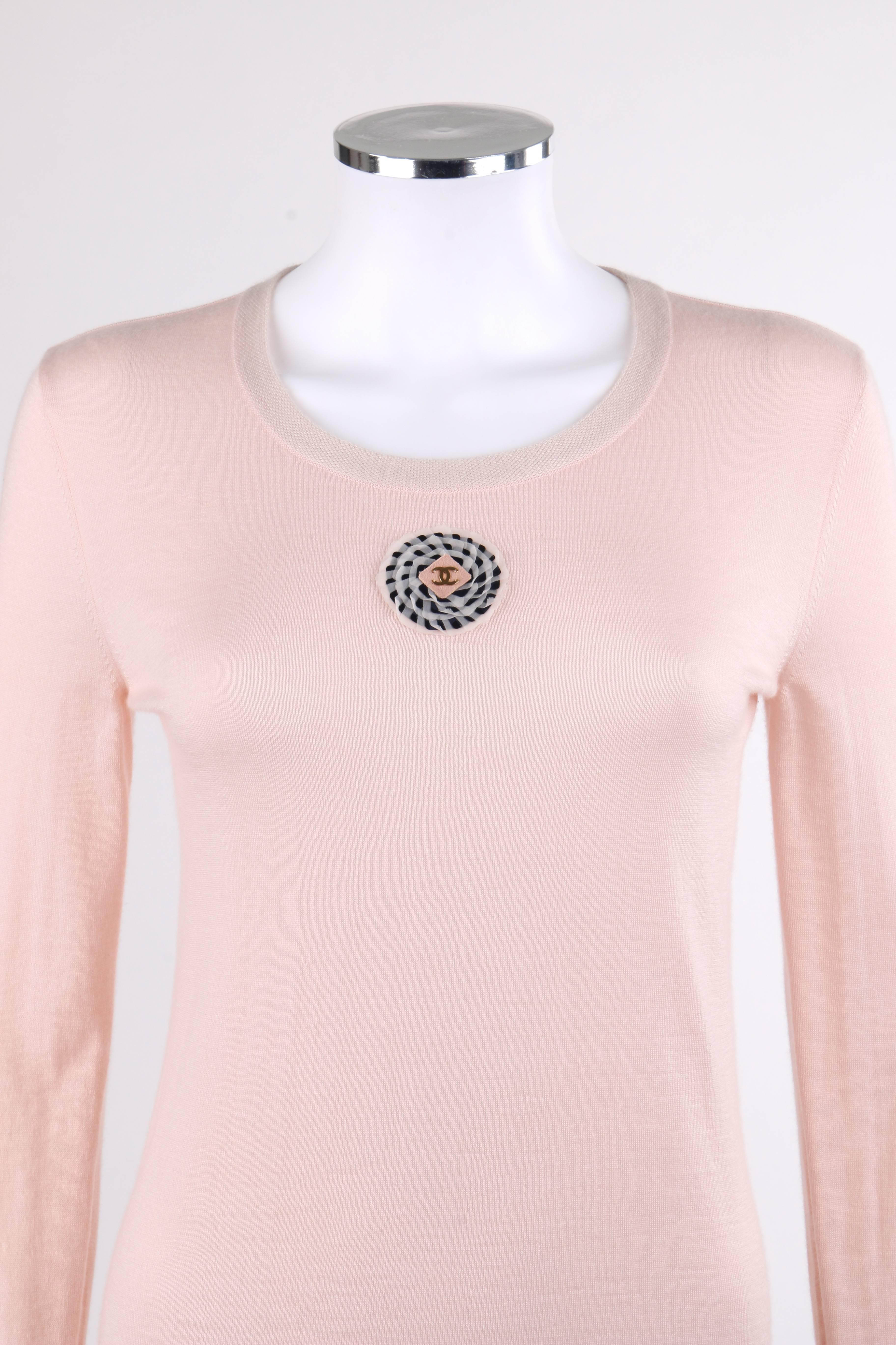 Chanel Resort 2011 Light pink cashmere and silk blend knitwear top. Center front black and white Camellia flower applique with centered gold-tone "CC" embellishment, Scoop neckline. Long sleeves. Pull over style. Marked Fabric Content: