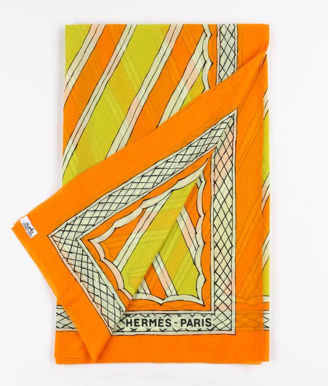 Hermes large orange and yellow cotton multi-use scarf. Orange, yellow, and winter white diagonal striped painterly design at center with scalloped edge. Winter white and back crosshatched boarder print. Orange background. 