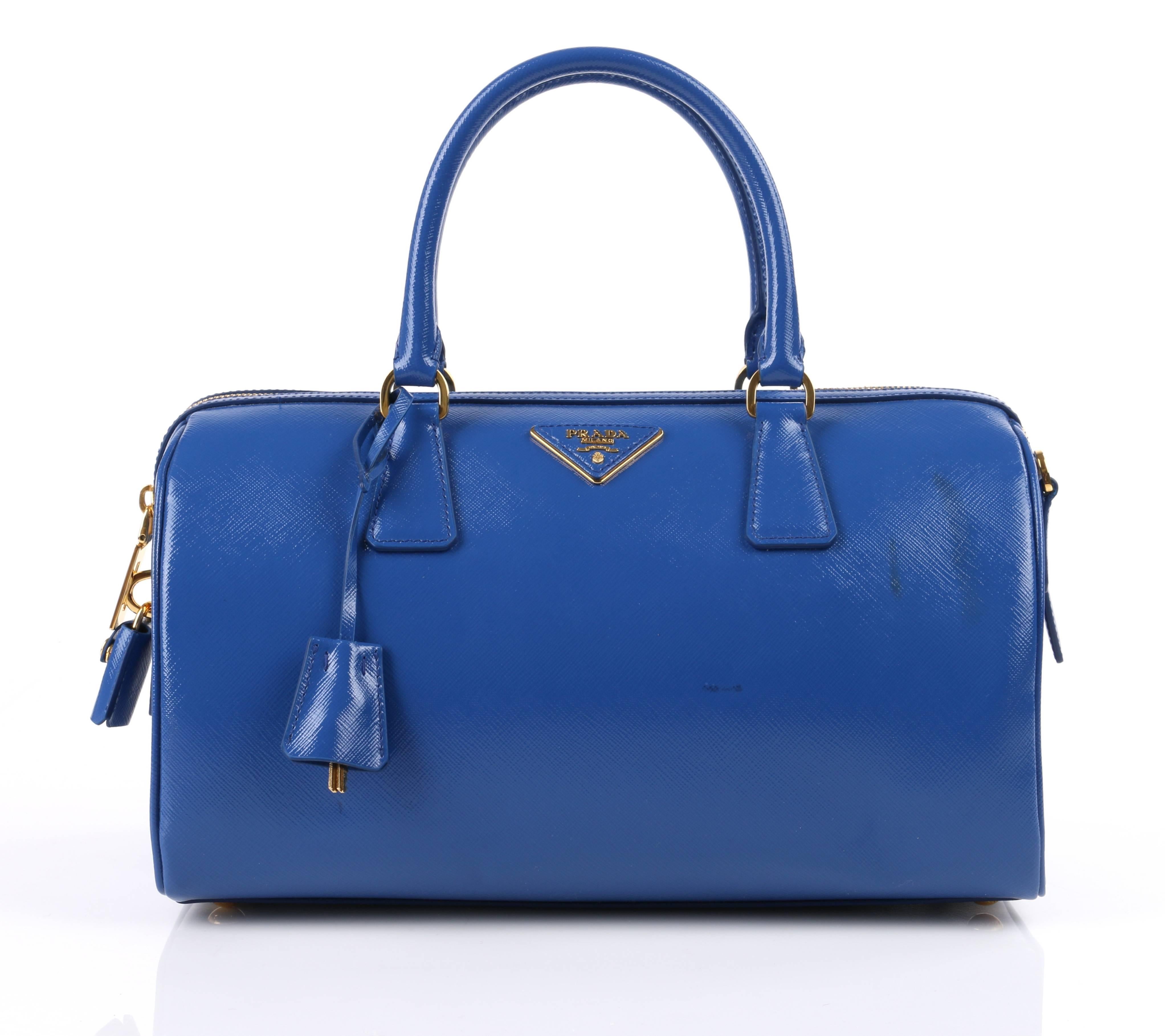 Prada Spring/Summer 2012 blue saffiano vernice (patent) leather convertible Boston bag. Designed by Miuccia Prada. Blue (azzurro) saffiano vernice leather structured body. Two single rolled top handles with gold-toned metal d-ring hardware. Piped