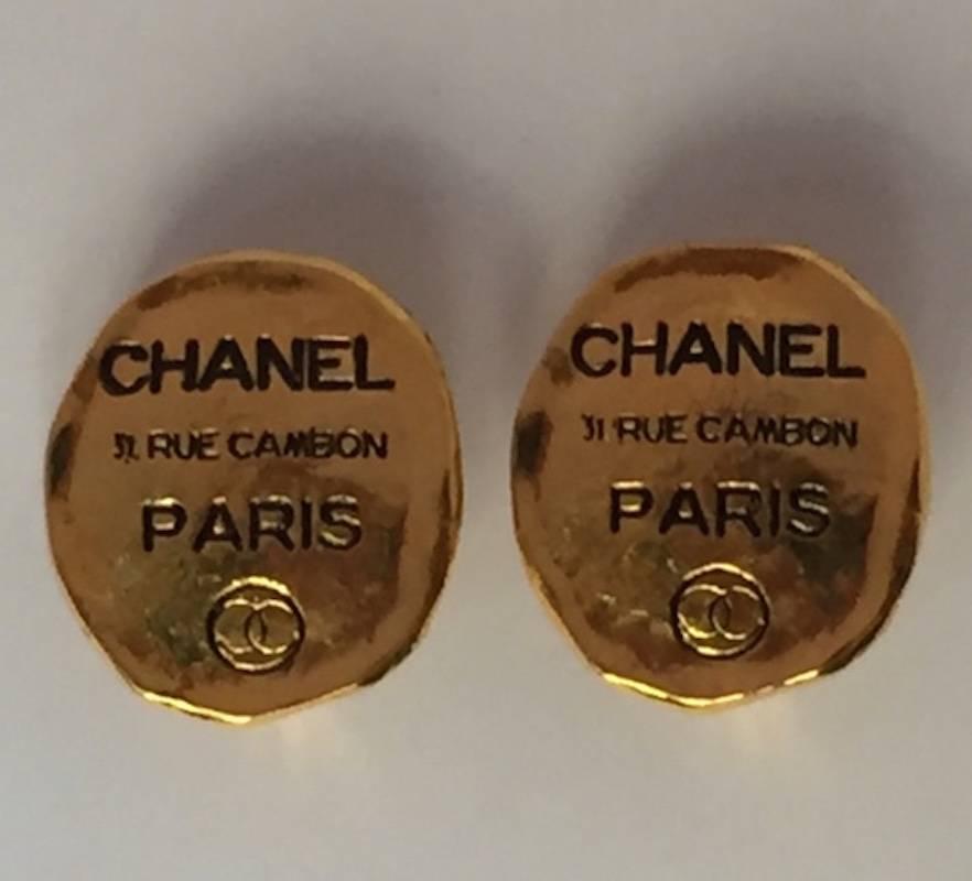 From the 1980s, this oval button style earring has a irresgular oval shape and like a was seal on a letter. Inscribed is Chanel and the address of the boutique in Paris with a small round double CC logo in circle. Each earrings measures 1 inch (2.5