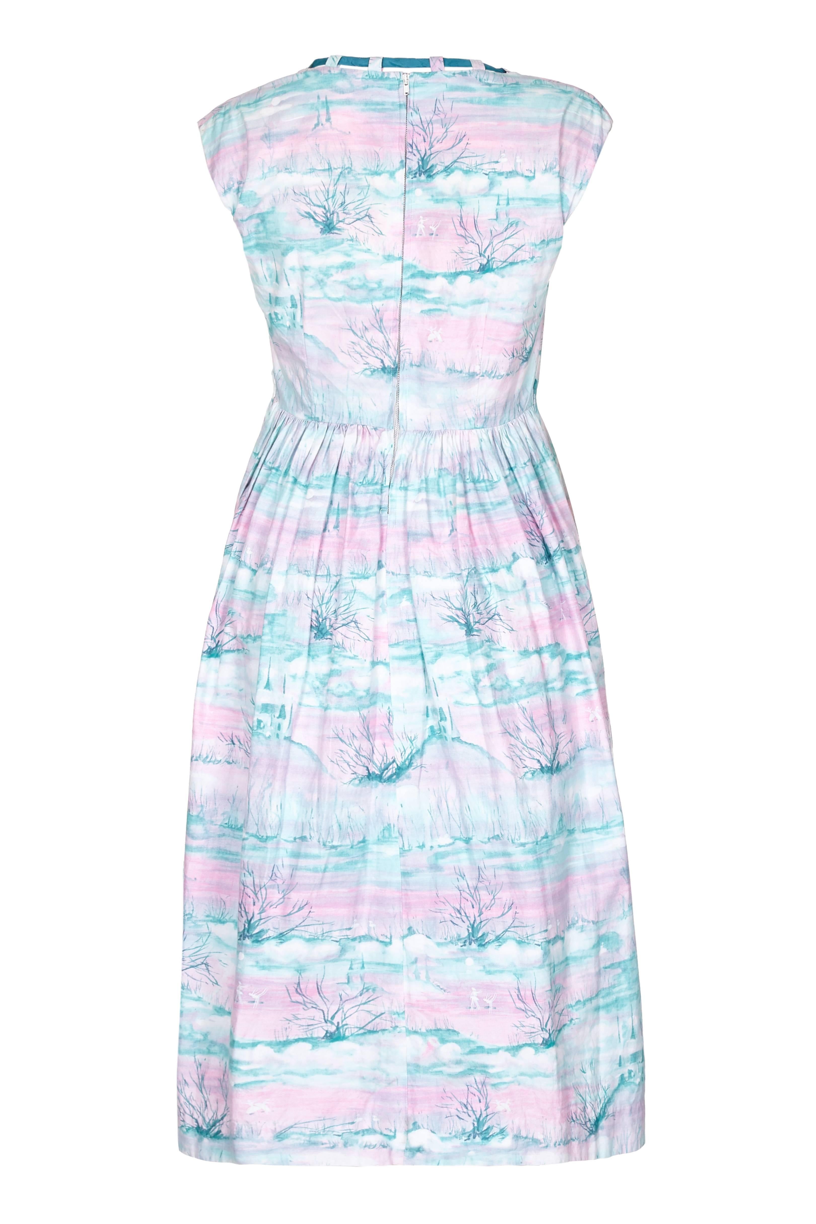 Amazing 1950s Swan Lake novelty print cotton day dress with teal coloured ribbon neckline. The print is in a pink and teal water colour featuring ballet dancers, swans on a lake, a castle and a forest.  This light weight dress is perfect for the