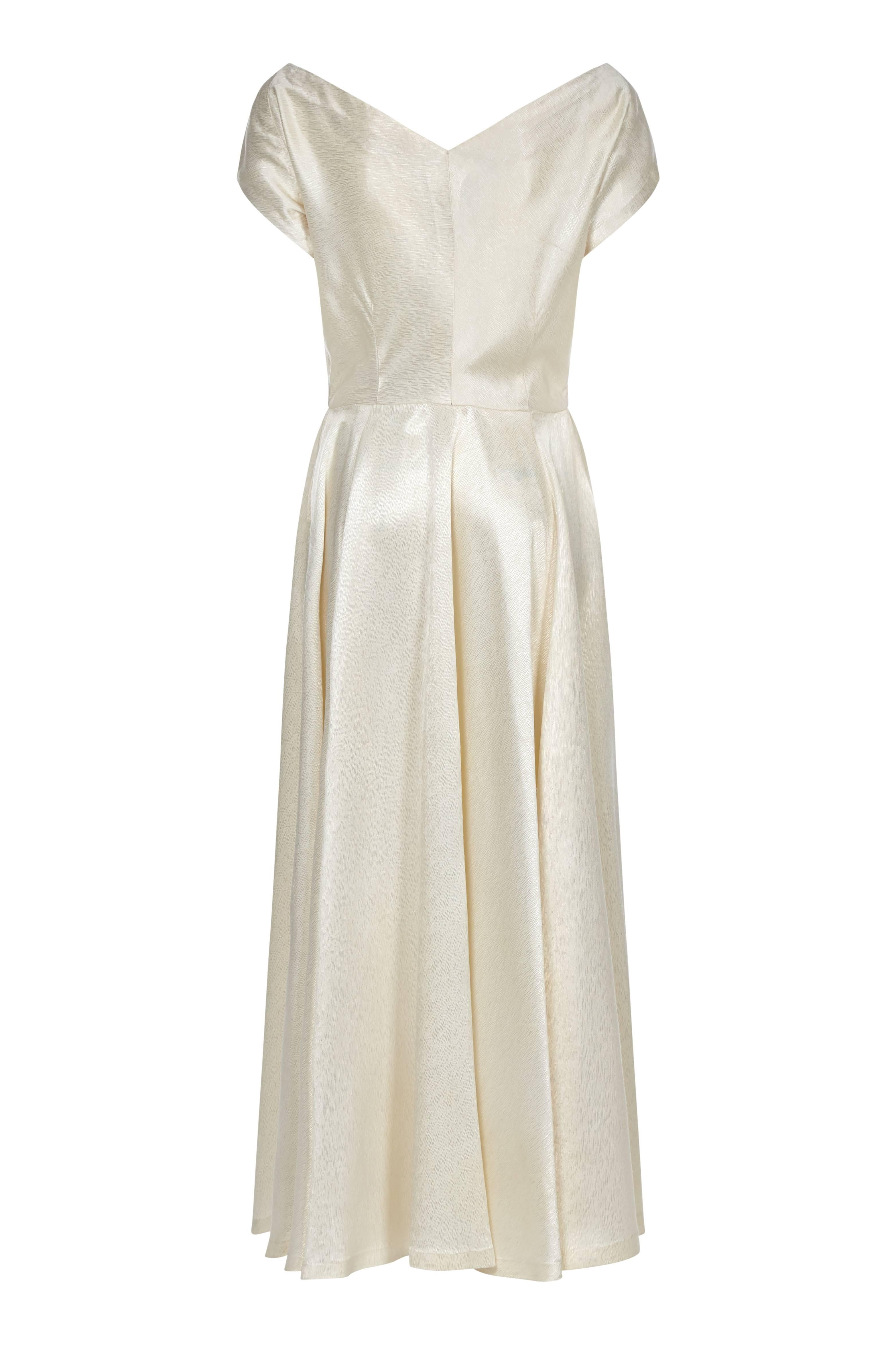 This elegant late 1940s pure silk ivory dress is a perfect example of the refined glamour of the era, its simple line skilfully accentuated by subtle detail in the construction. The thick, delicately embossed silk is a warm Ivory tone, and its