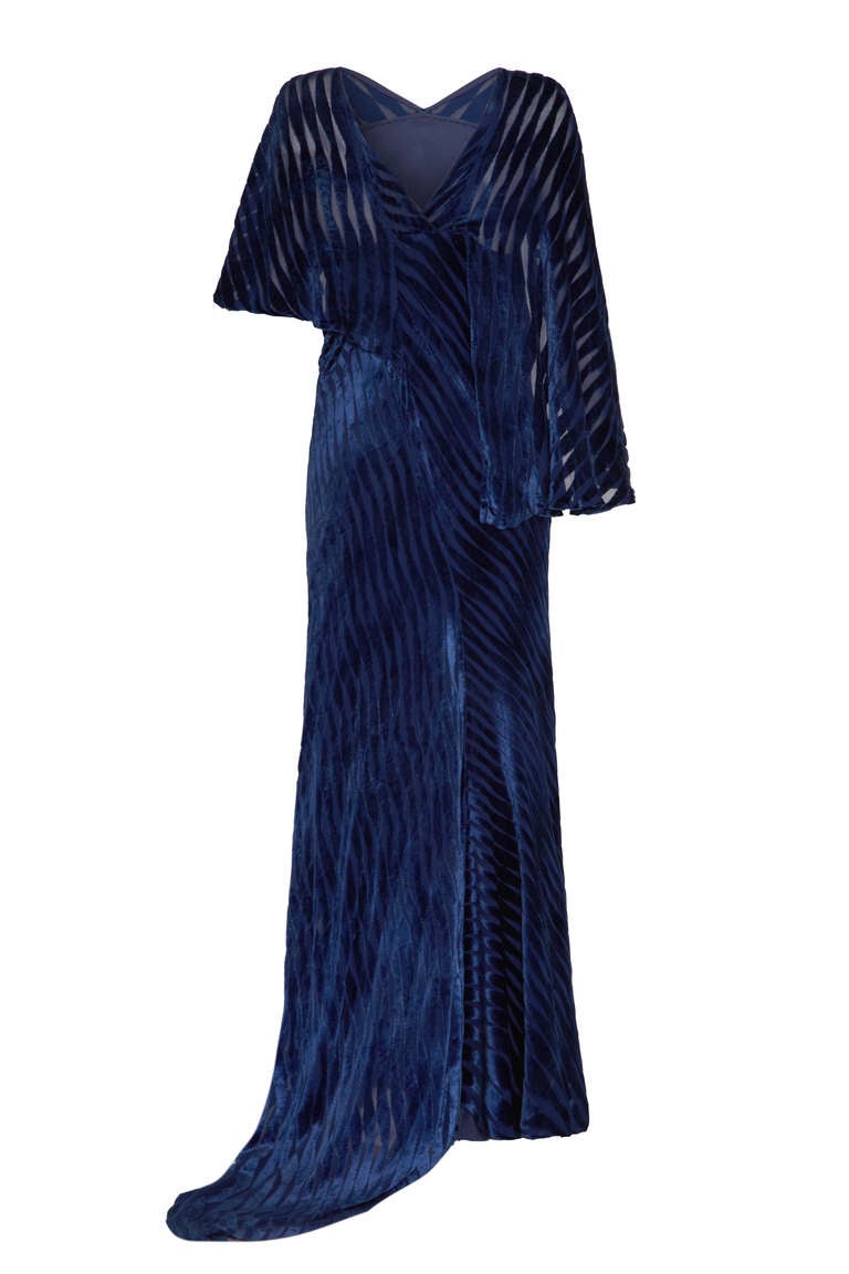 This is a truly sensational gown in a rich royal blue velvet with a striped burn out pattern. The unique asymmetrical design features a slightly off centre train and cape style sleeves in different lengths. The main body of the dress features a V