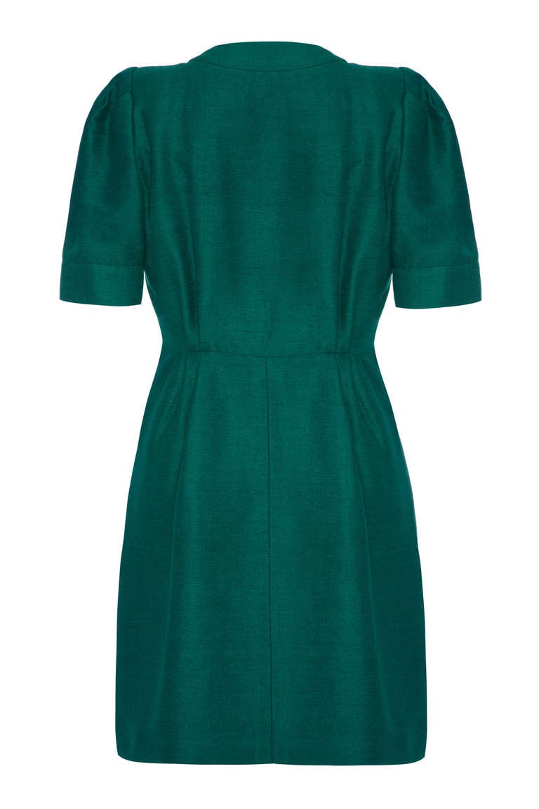 A gorgeous green silk dress from Yves Saint Laurent. This simple yet stylish piece features short puff sleeves, pockets on the hips and is lined in a coordinating green. Large blue and gold glass button fasten up the asymmetrical front opening and