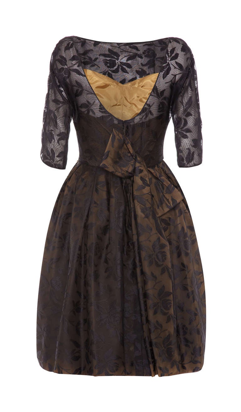 Simply gorgeous black cocktail dress with unusual details. This elegant peice is made up of a sheer back organza with a floral and leaf print with a gold shaped and boned interior.  It features ¾ sleeves, low neckline at the back and a large off