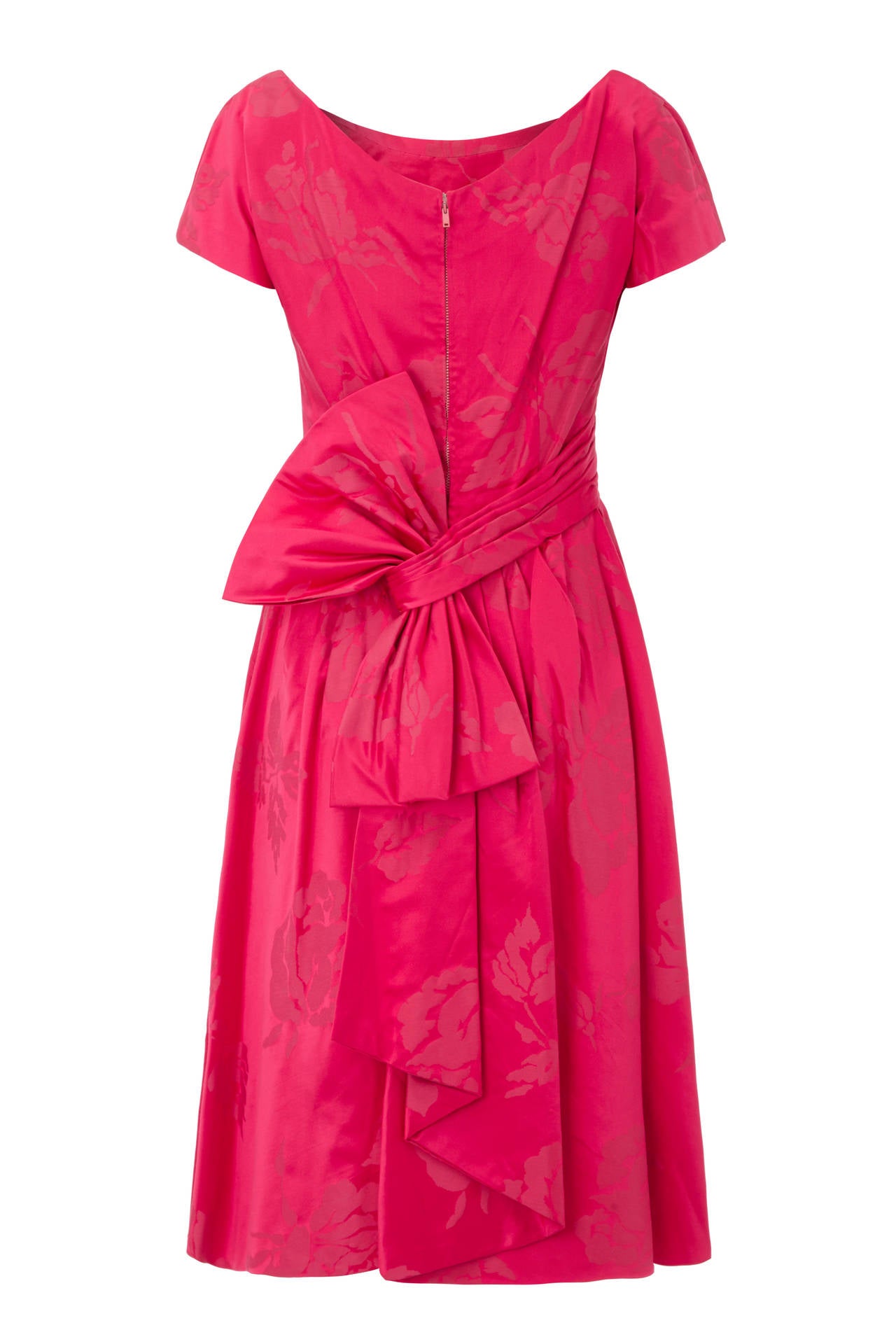 Beautiful pink silk party dress with large rose brocade pattern. Unlabelled and reminiscent of Christian Dior designs, this fun piece features a scoop neckline, cap sleeves and a large bow detail at the back.  It is fully lined in organza, fastens