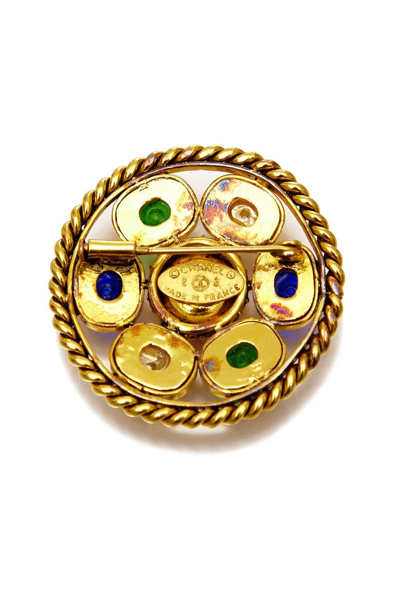 Lovely vintage brooch designed by Victoire de Castellane for Chanel.  It consists of a twisted gold tone metal outer ring with six mounted stones in pearl and green and blue gripiox glass around a larger central red gripoix glass stone. Stamped on