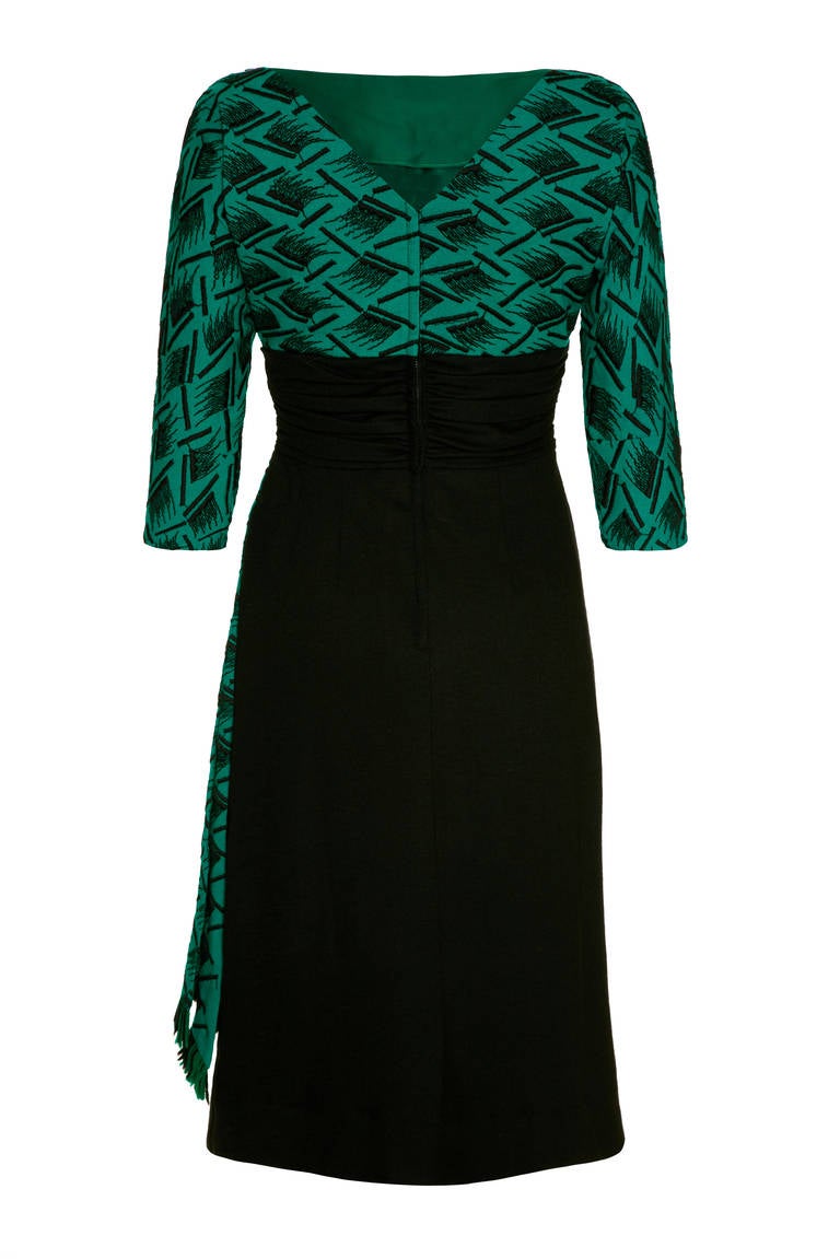 Fantastic 1950s dress with a black wool jersey pencil skirt and gathered waistband with a contrasting emerald green wool bodice and tassled section over the skirt.  The dress features Pretty ¾ sleeves and a boat neckline with a deep V at the back. 