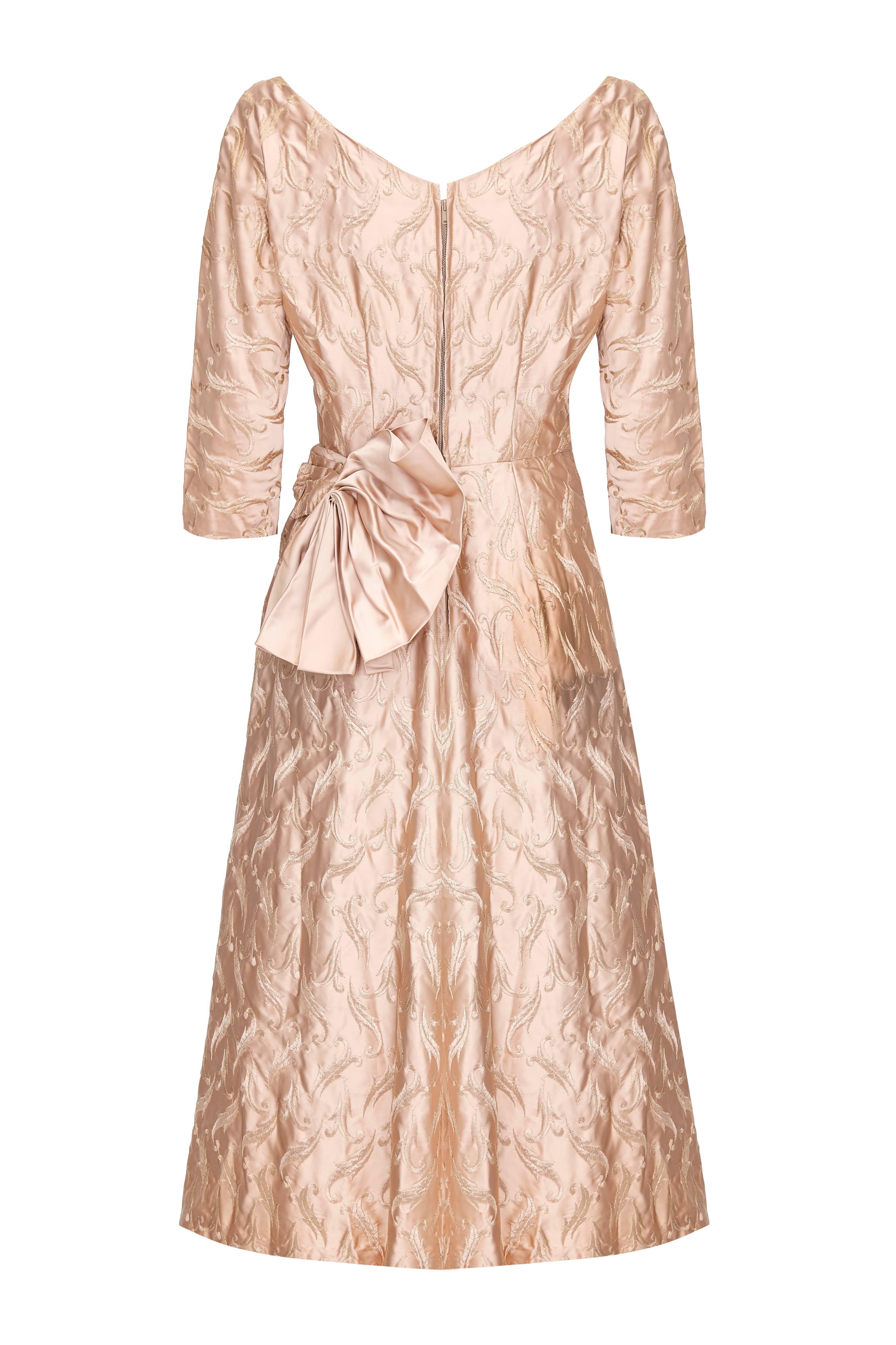 Beautiful vintage 1950s American dress in antique rose gold silk with embroidery.  This lovely piece features ¾ sleeves, net inside the skirt for extra volume, a pleated bow and zip fastening at the back. It is in excellent condition with no