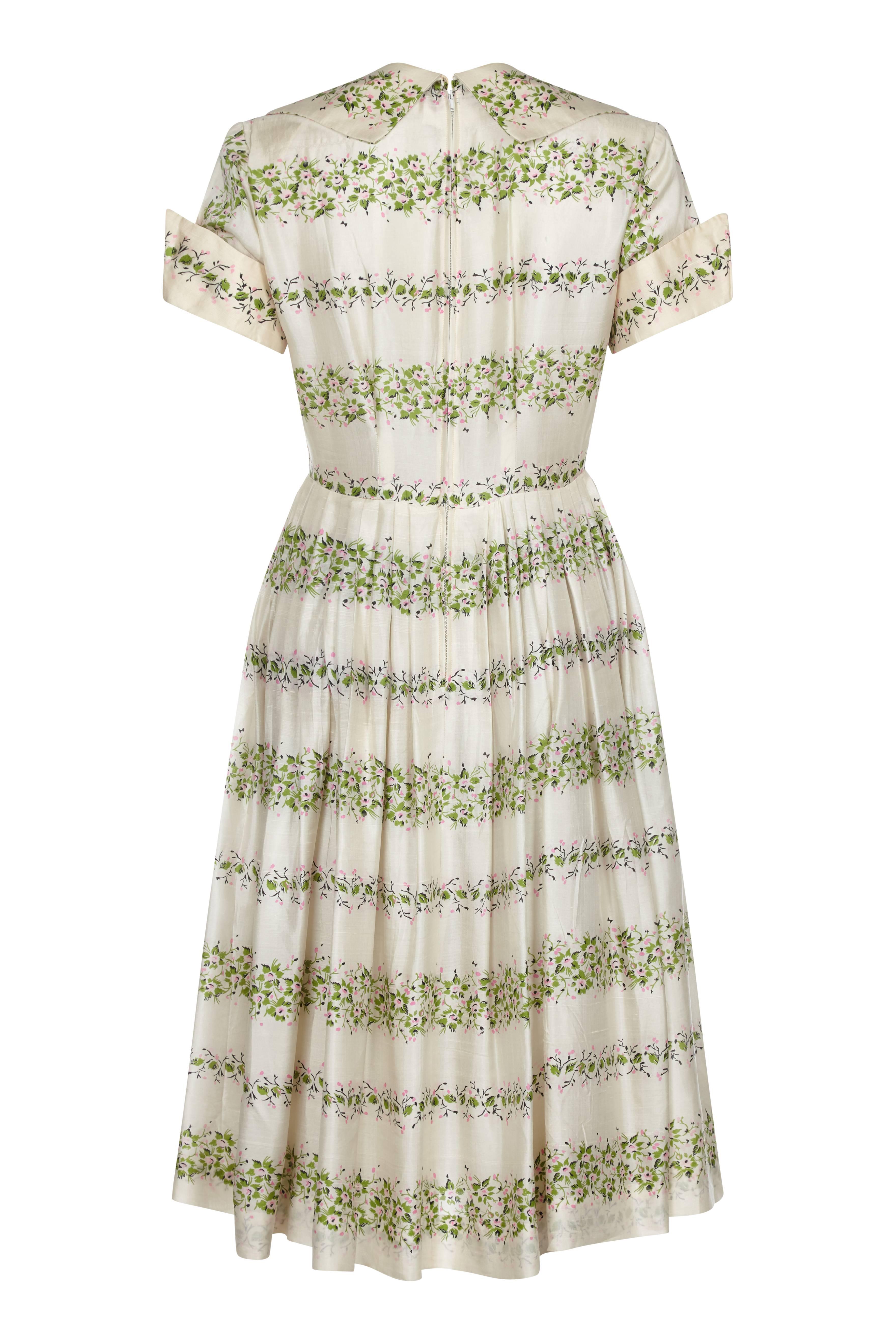 This effortlessly pretty 1950s pure silk day dress embodies the spirit of spring/summer. The colour is predominantly cream, with a light pink and green floral motif that runs the length of the dress in soft horizontal stripes. A classic 1950s cut,