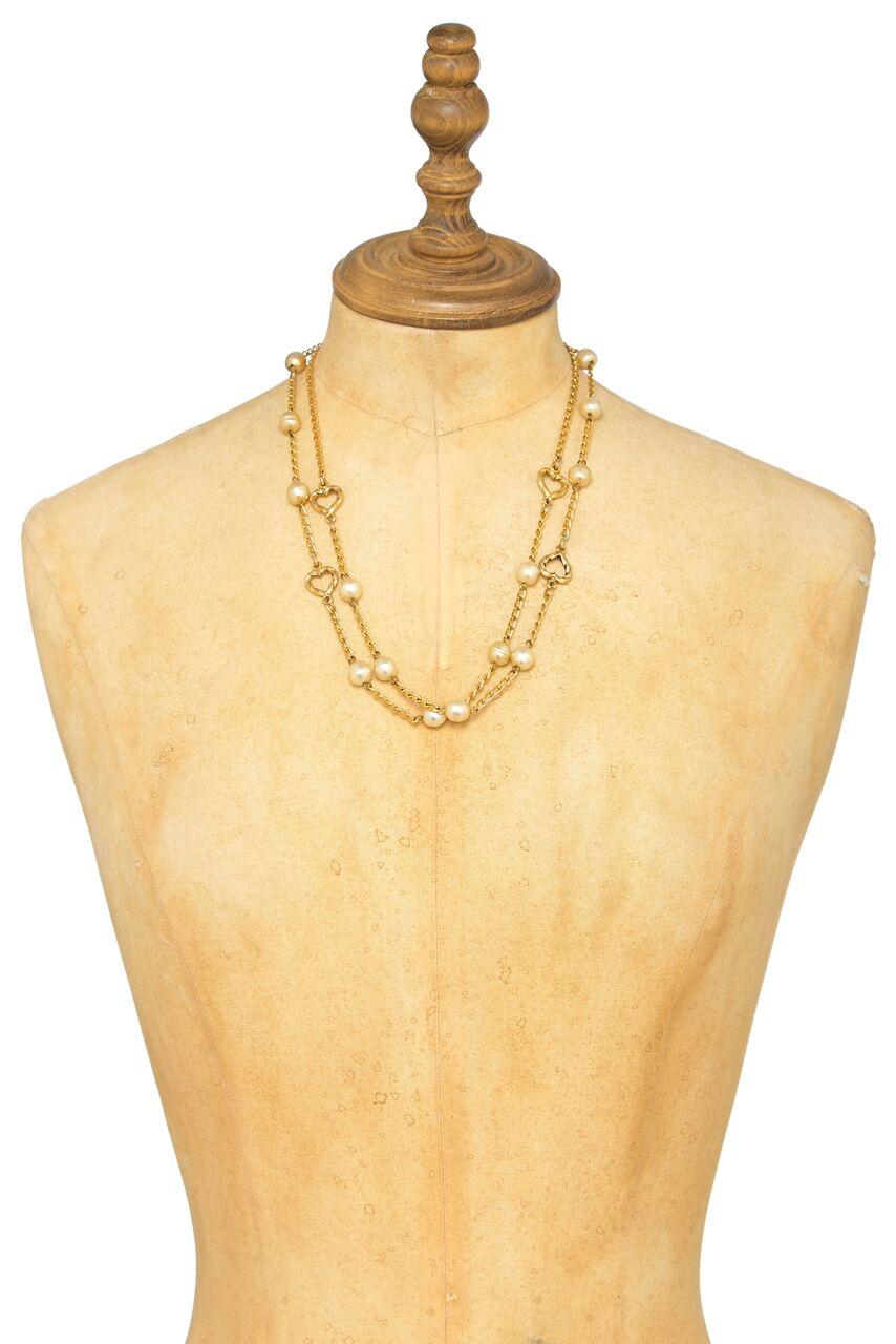 This Chanel mid 1980s gold tone Sautoir necklace with faux pearl lustre beads and gold tone heart shaped charms is in lovely vintage condition. Can be worn at full length or doubled over if desired. There is a round clip fastening emblazoned with
