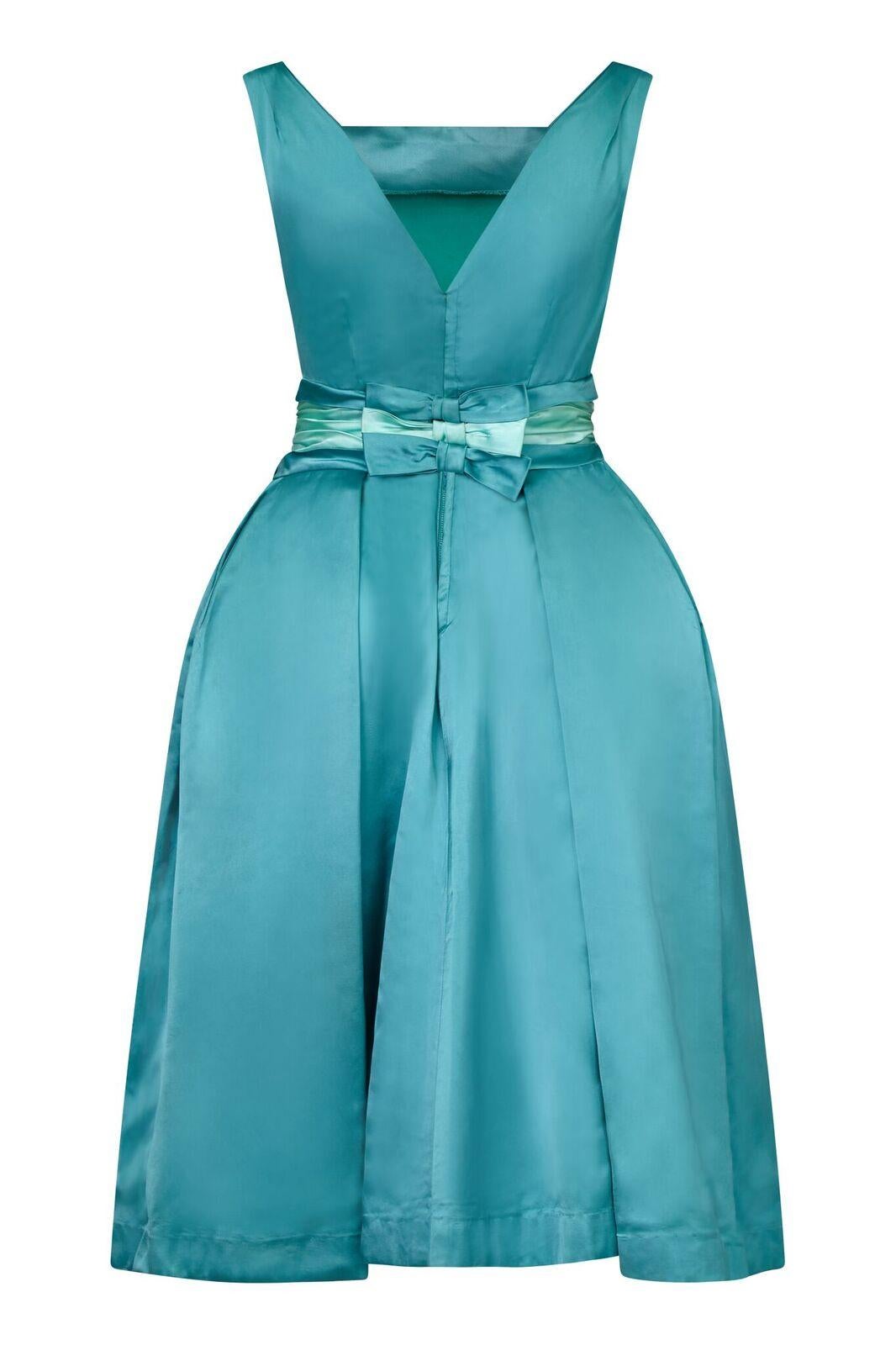 This spectacular duchess dress in turquoise satin has magnificent construction and emulates the extravagance and glamour of the 1950s. The sleeveless bodice has a subtle square neckline at the front, and graduates in a V at the reverse. The wide 4.5