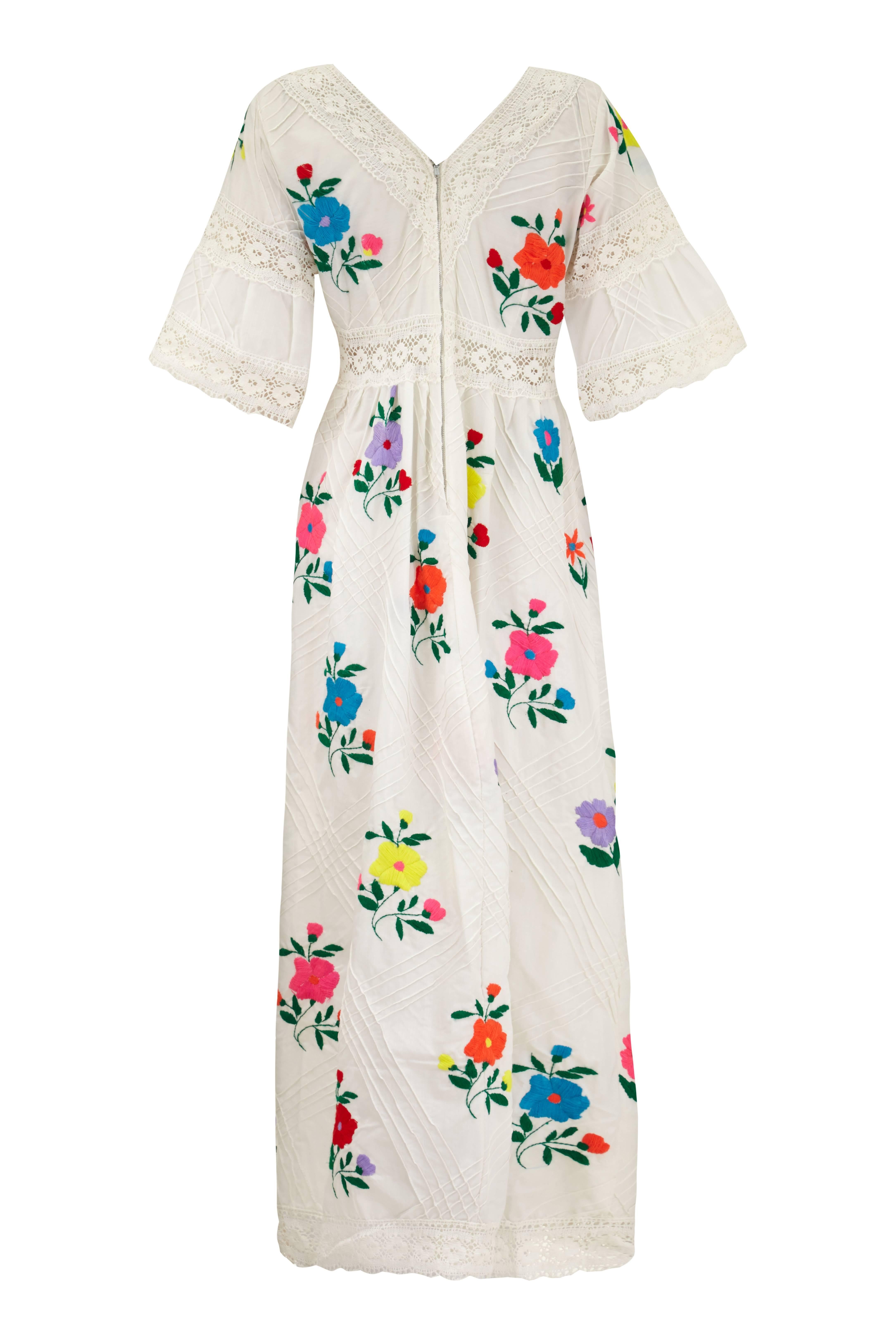 Beautiful original 1970s vintage white cotton Mexican wedding dress with pintucking, lace inserts and trim throughout.  This example features pretty and bold colourful woolen floral embroidery and has fluted elbow length sleeves. There is a