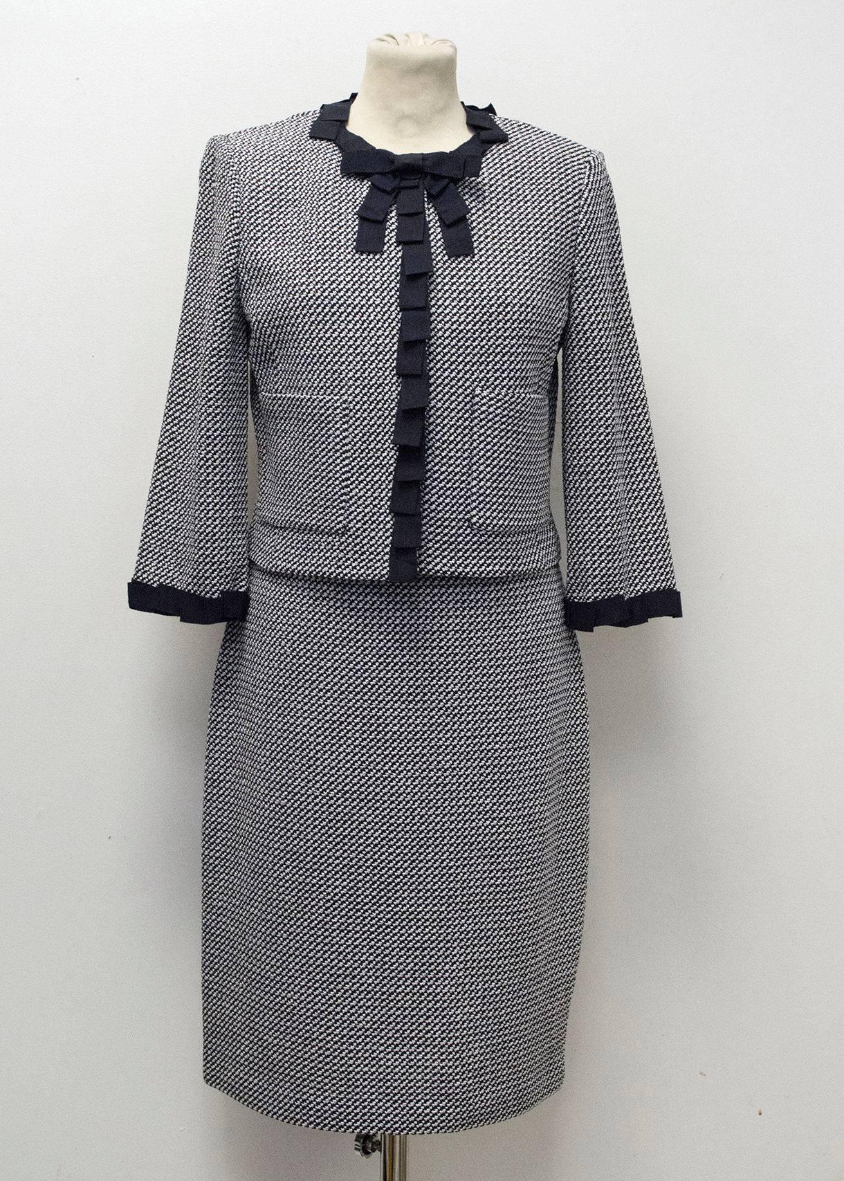 St. John dress and jacket in a navy and white houndstooth pattern. The dress is sleeveless and fitted with square-v neckline, navy ribbon detail on the vest and concealed zip closure at the back. The jacket is unlined with a relaxed fit and is