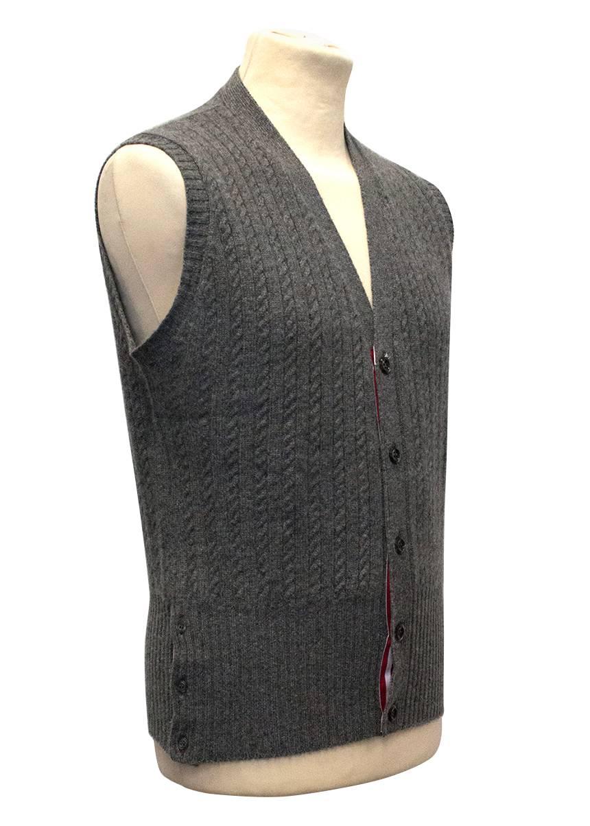 Thom Browne grey cashmere cable knit vest. The vest is slim fitting and sleeveless featuring a ribbed design, V-neck collar, front button closure, functioning button detail on the hips and red, white & blue grosgrain interior trim. Size