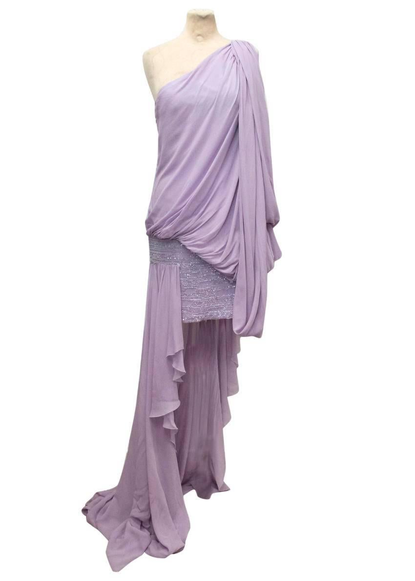 Elie Saab lilac one shoulder silk dress featuring a beaded, embellished mini skirt and a draped waterfall train with embellished detail on the shoulder and draping detail to the shoulder, hips and back. The dress is light weight and soft to the