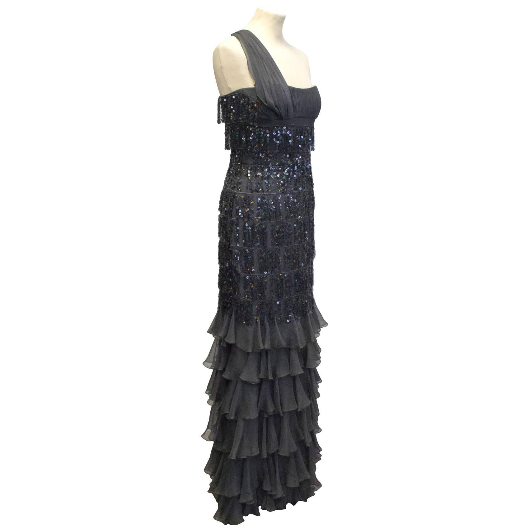 Jacques Azagury charcoal grey evening dress. This dress features a one shoulder strap, a sequinned tassel bustier and long flowing tiered ruffle skirt. 

The dress is fastened by a concealed zip at the back and a small clasp on the inside of the