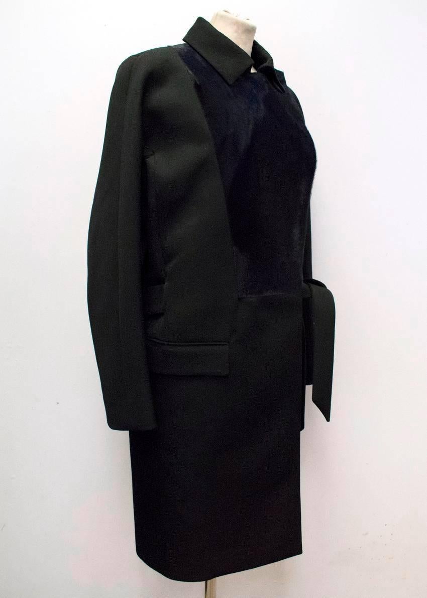 Salvatore Ferragamo black long coat with a navy blue lambs fur panel on the front of the jacket. The coat is double breasted, has a spread collar, a stitched belt, two pockets on the front and a single vent at the back of the coat. Lined with 65%
