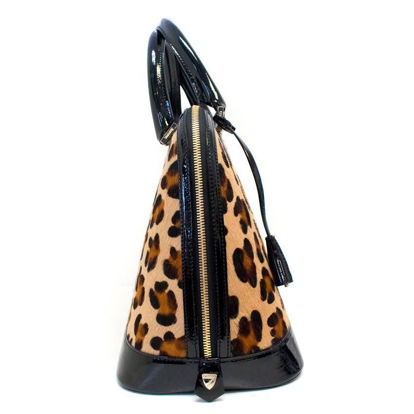 Aspinal of London leopard print pony hair handbag rimmed with black patent leather and featuring gold toned hardware details including a zip and an attached padlock with engraved brand name and a key.
The inside is lined with red cotton blend and