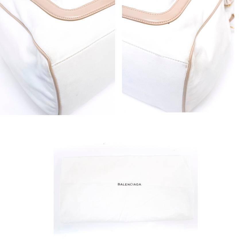 Balenciaga white leather tote with beige accents at the top, handles, and on the front exterior magnetic buttoned pocket. It also features gold hardware on the front zipper pocket, the handles, sides and the lock closure. There is also black lining