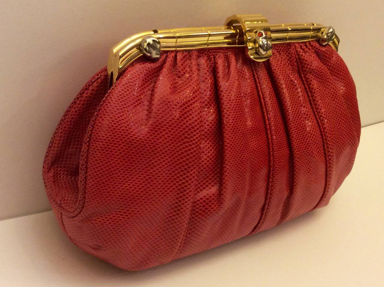 This is a gorgeous Judith Leiber clutch with optional chain. The handbag is composed of a striking red lizard with gather details. There are two interior slot & zipper compartments and snap closures, and gold hardware and 3 small frog detail.