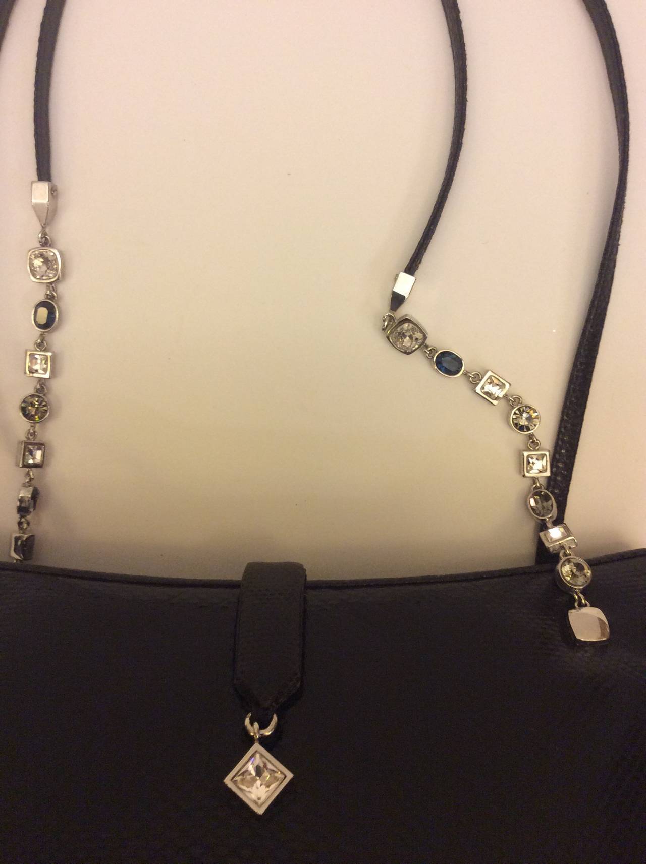 This is a gorgeous Judith Leiber black lizard tote. There are two main interior compartments. Double strap lizard handles with silver chain crystals  & sapphires. 

Measures (Approximately)
Height: 4