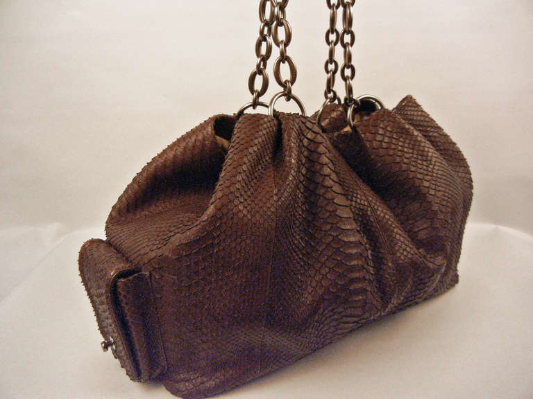 This roomy Bvlgari chocolate python leather hobo bag has two handles and silver tone chain-like hardware. Closures consist of a magnetic catch and a button closure. Outside there are two magnetic exterior pockets. Inside there is one interior zipper