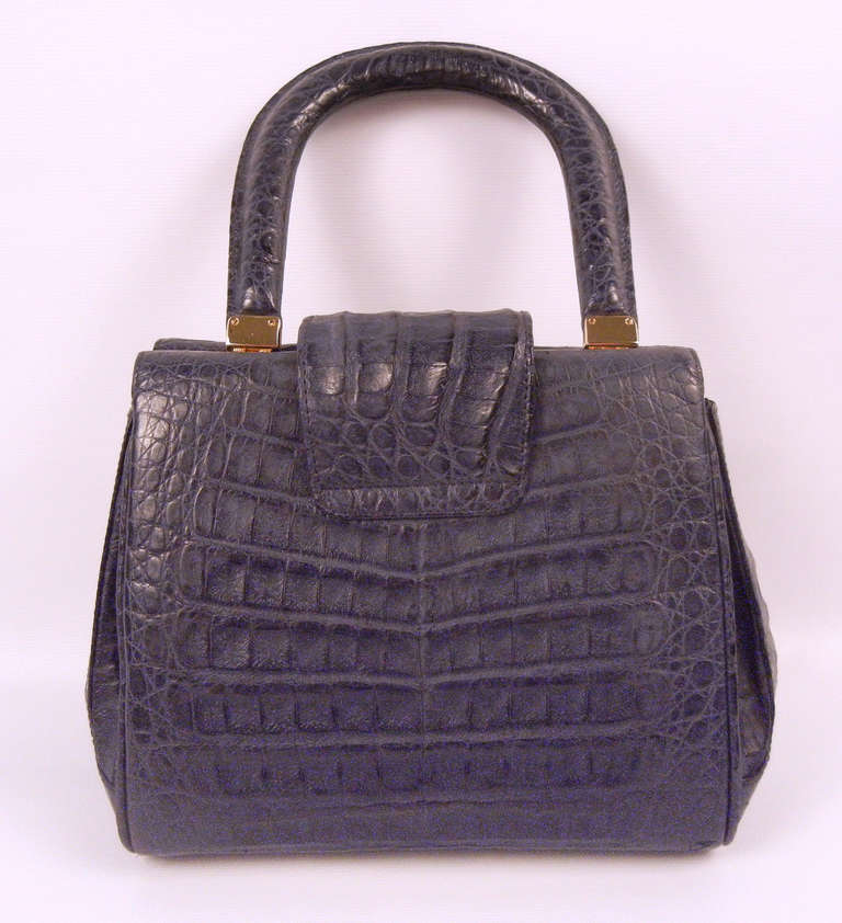 This Lana Marks one-handle navy crocodile leather purse is a beautiful addition to one's purse collection! Interior divided into two sections. Complete with gold hardware, one interior zipper pocket, and two interior flap pockets. Exterior magnetic