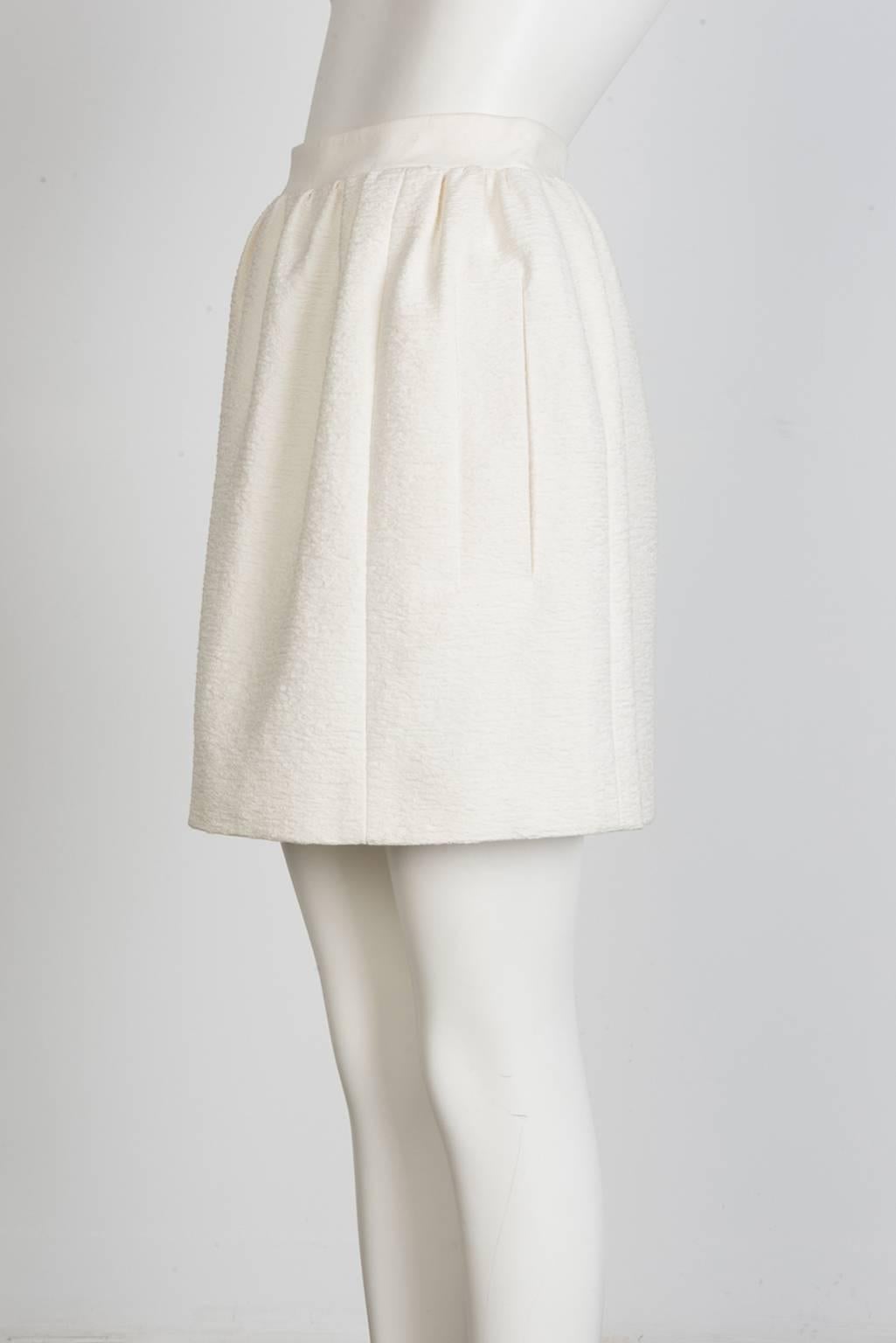 Structured, pleated mini skirt in stiff silk with slash pockets and pale pink zipper detail.