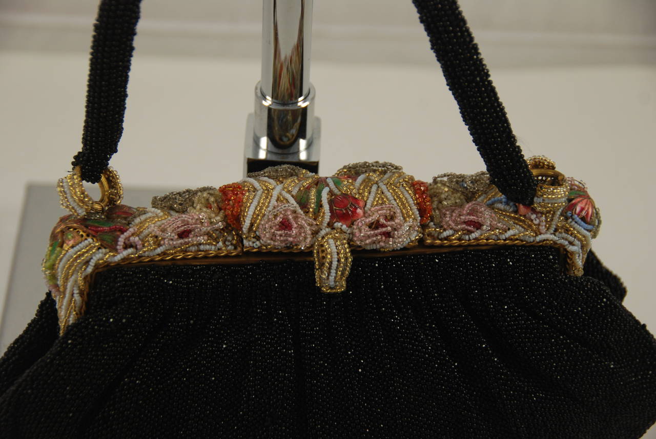 WOnderful example of the beaded handbags produced in France post WWII. The body of the bag is done in black beads that flimmer in the light and the frame is a combination of beading and enamel work. Even the rings that attach the strap to the bag